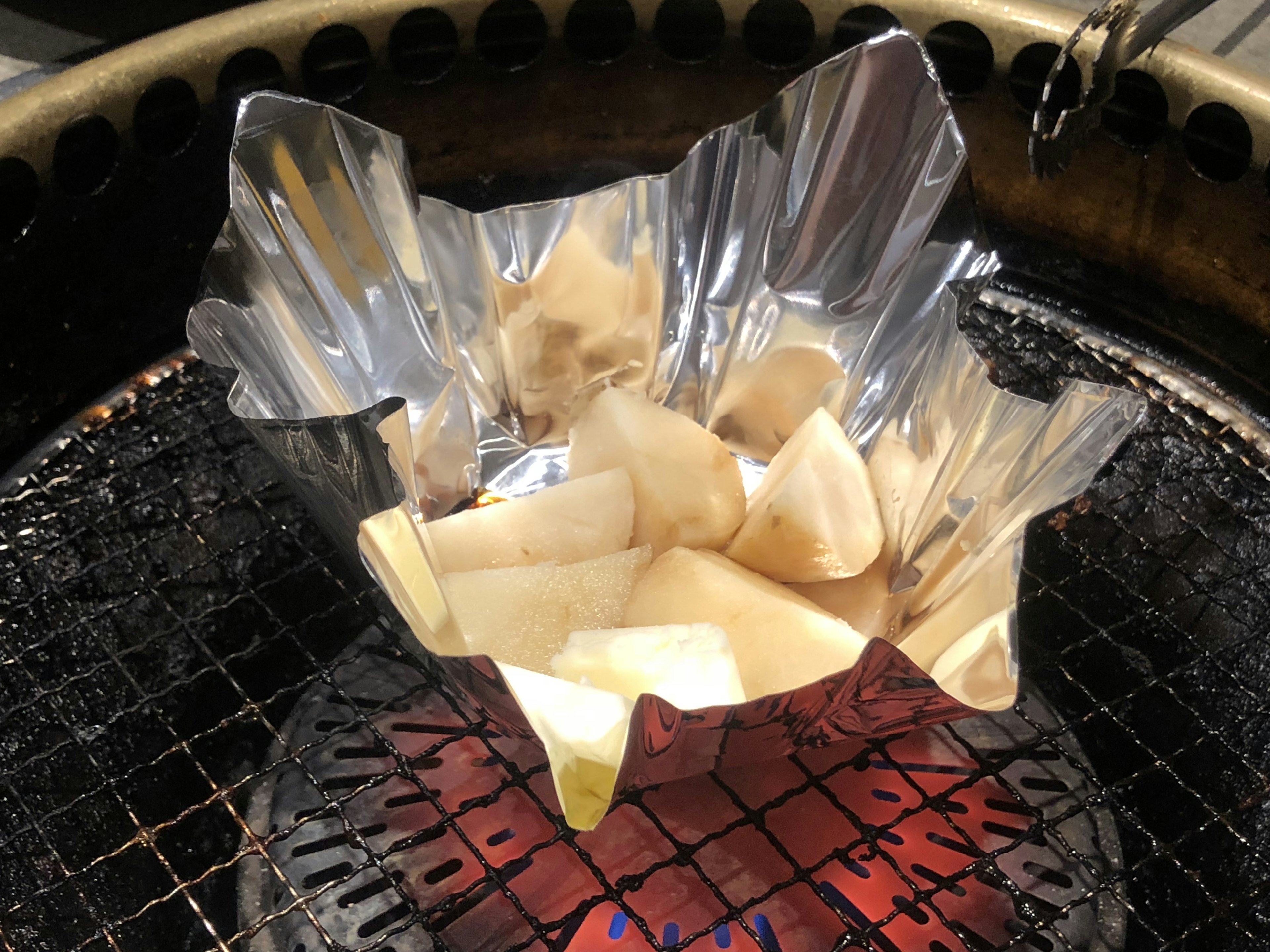 Aluminum foil bowl with food cooking over charcoal