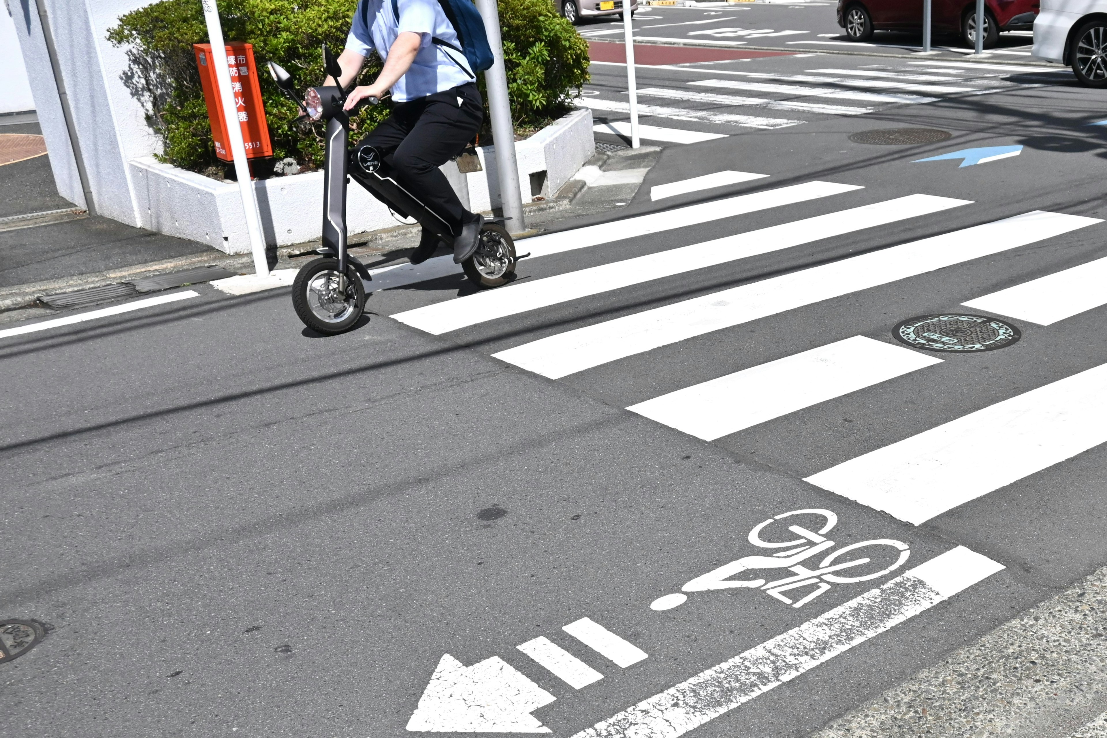 Conducteur sur une trottinette électrique traversant un passage piéton avec un indicateur de piste cyclable