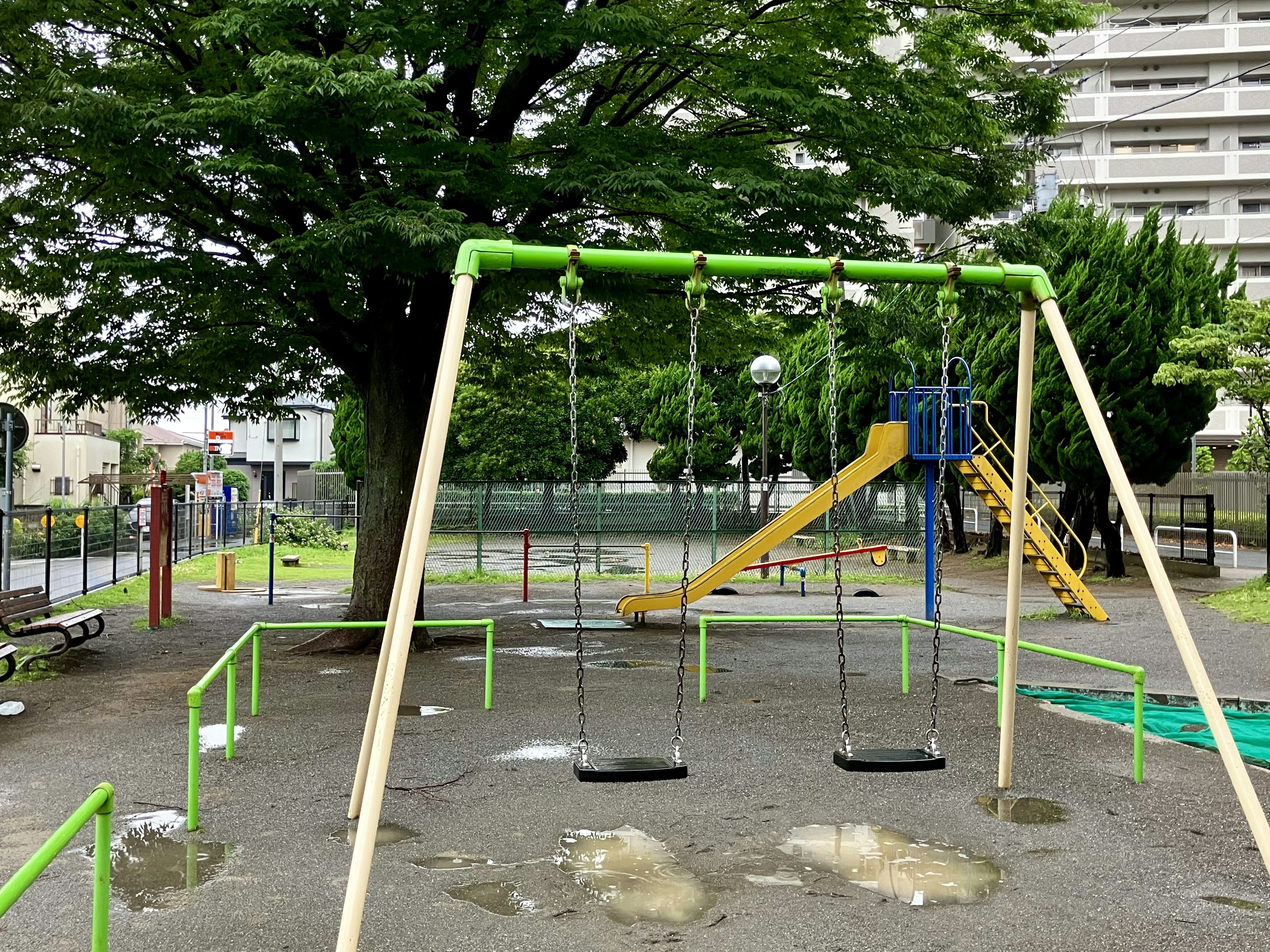 公園のブランコと滑り台のある遊び場 緑のフレームと大きな木が特徴