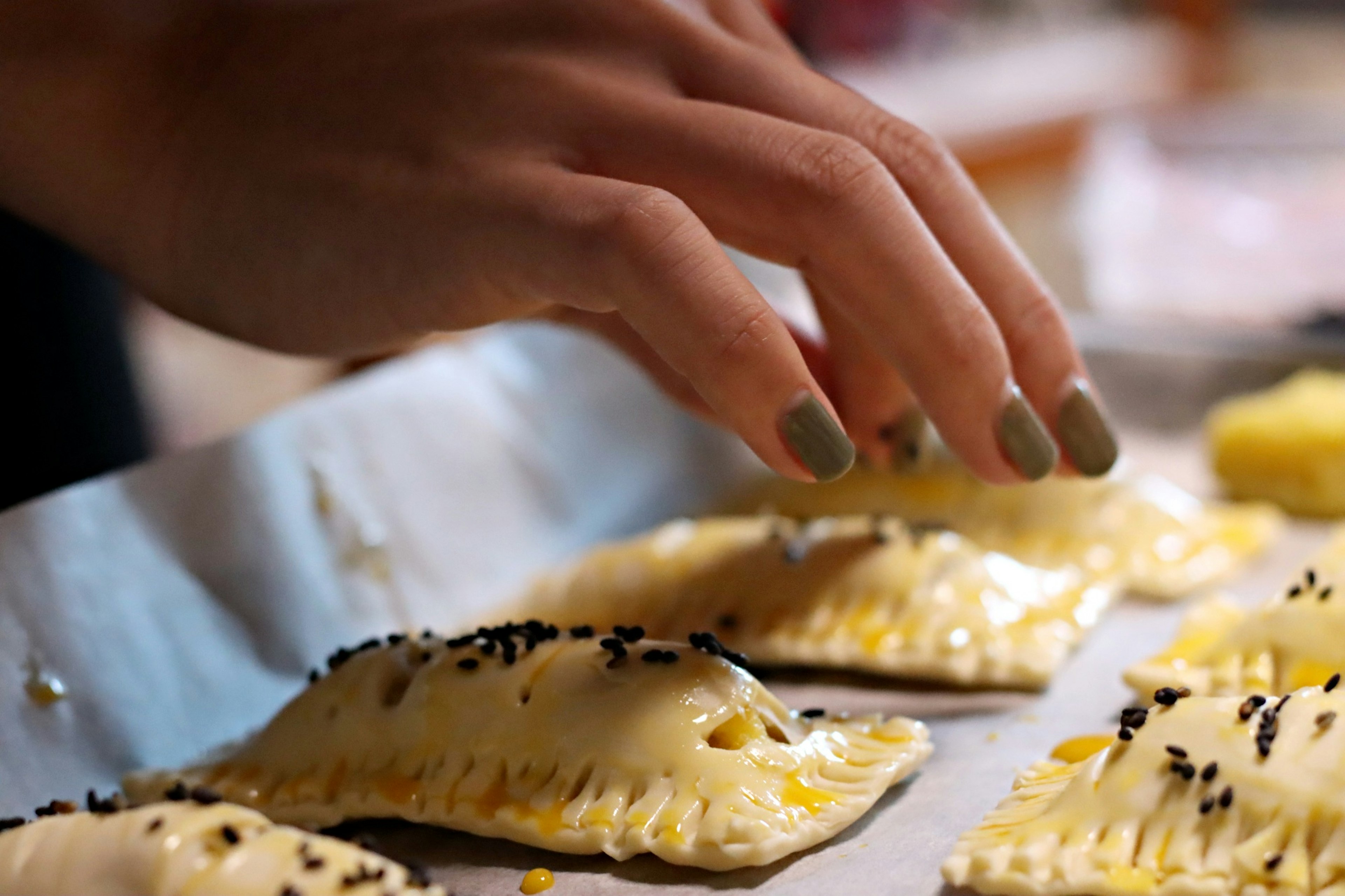 Hand reaching for baked pastries topped with sesame seeds