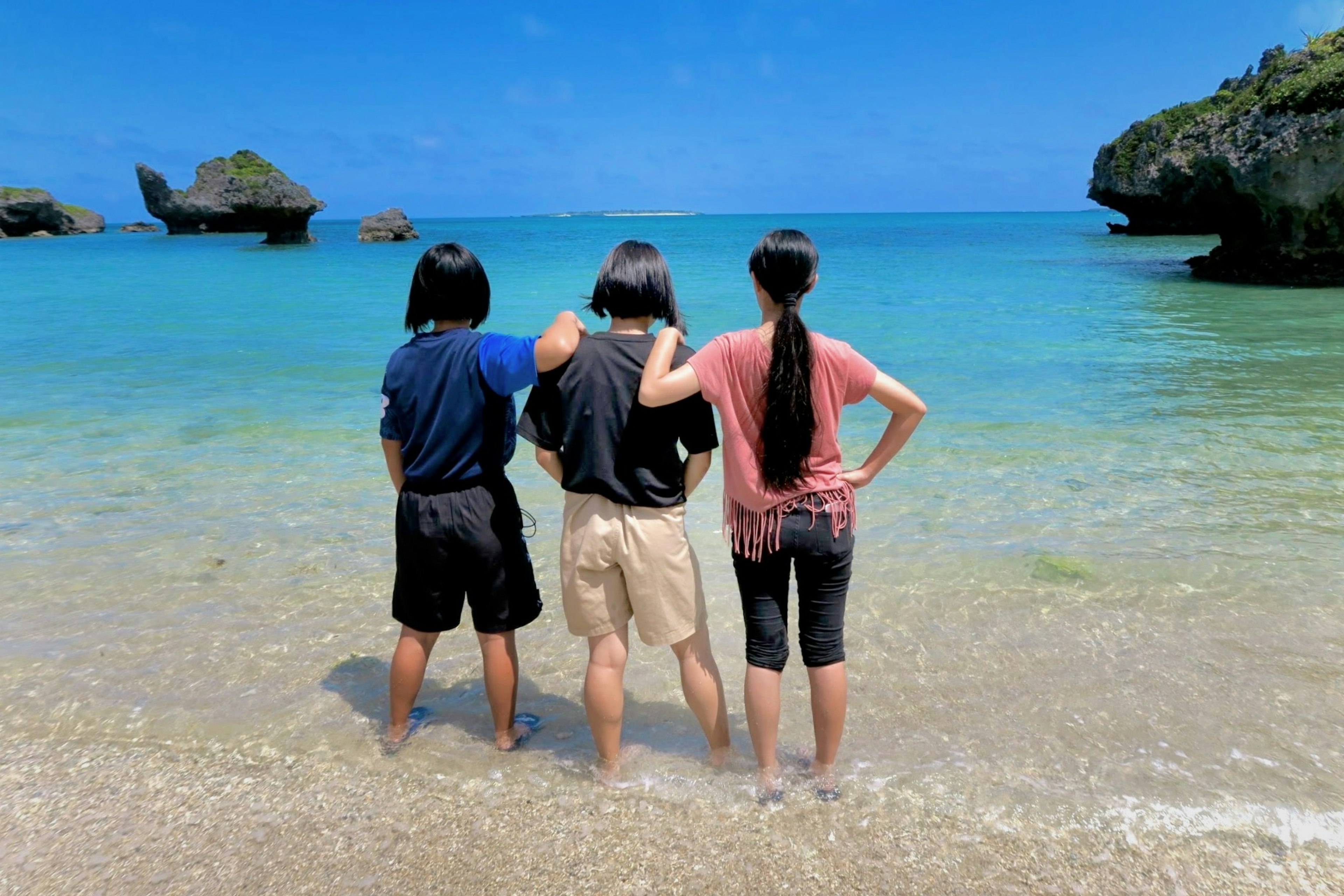 Drei Freunde stehen am Strand und schauen auf das Meer