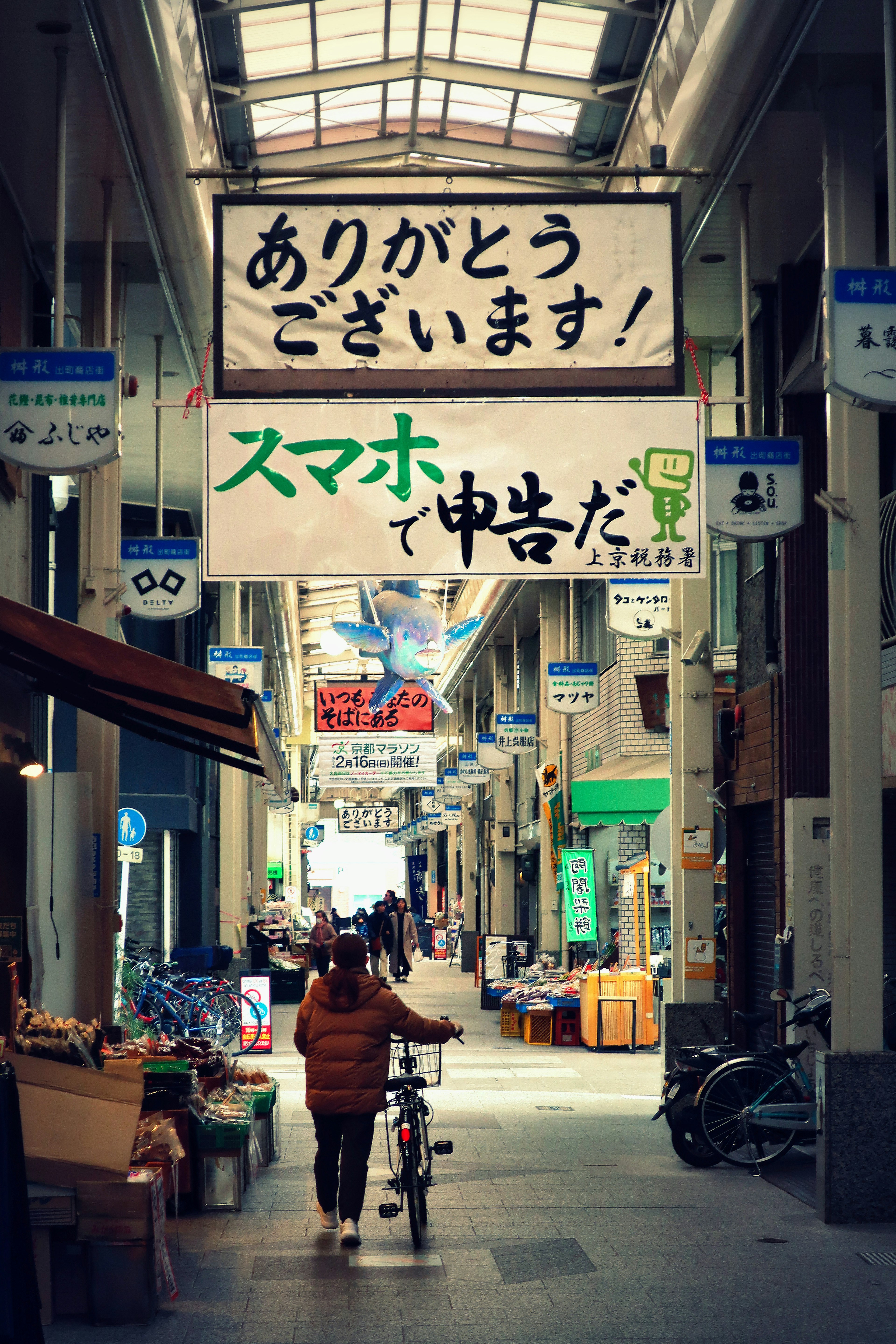 商店街の通りに自転車を押して歩く人と日本語の看板