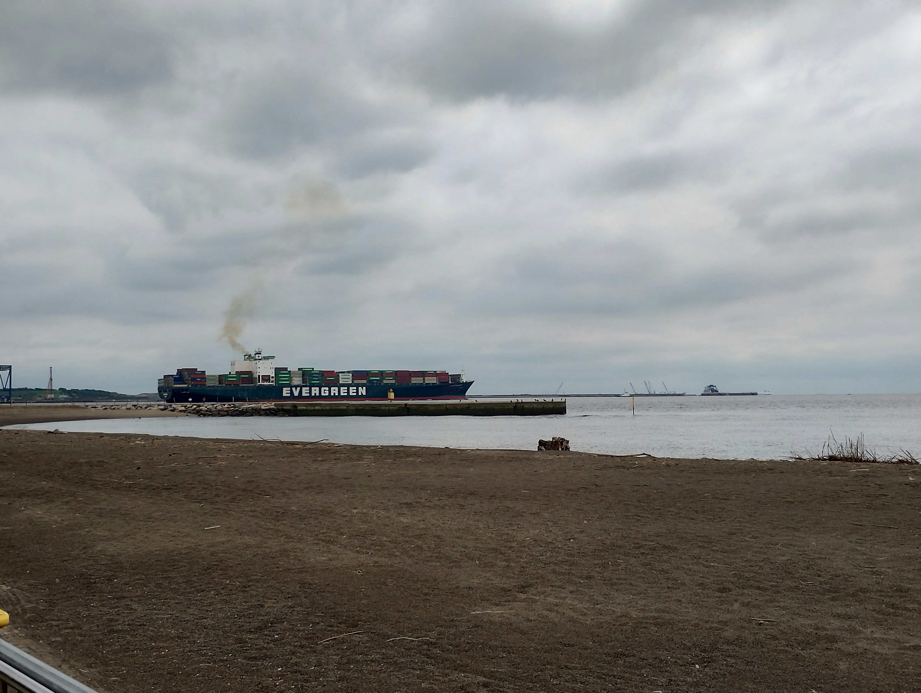 A gray sky over a ship docked at the shore with a sandy beach