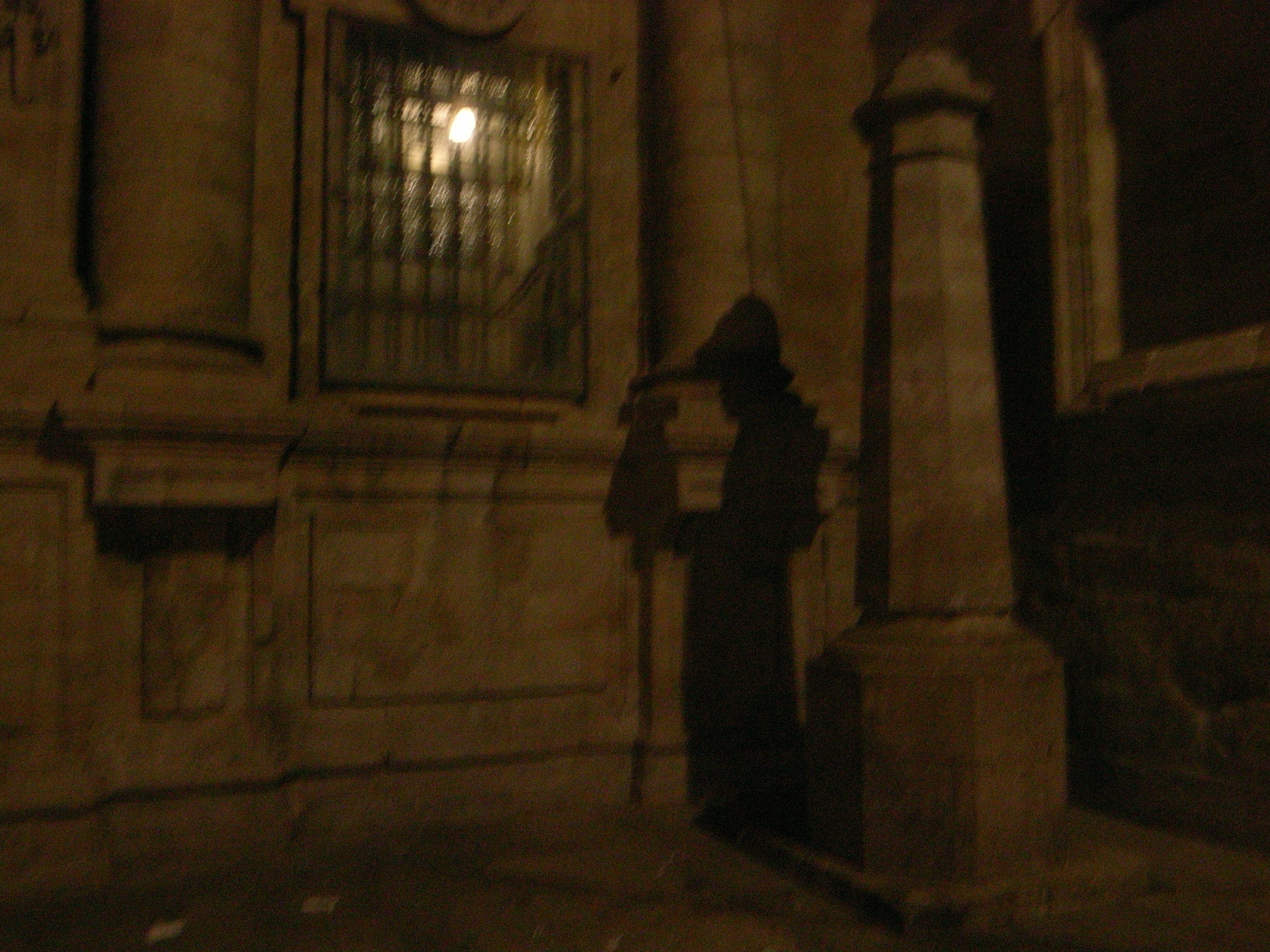 Silueta oscura junto a una columna de piedra y una ventana con barrotes