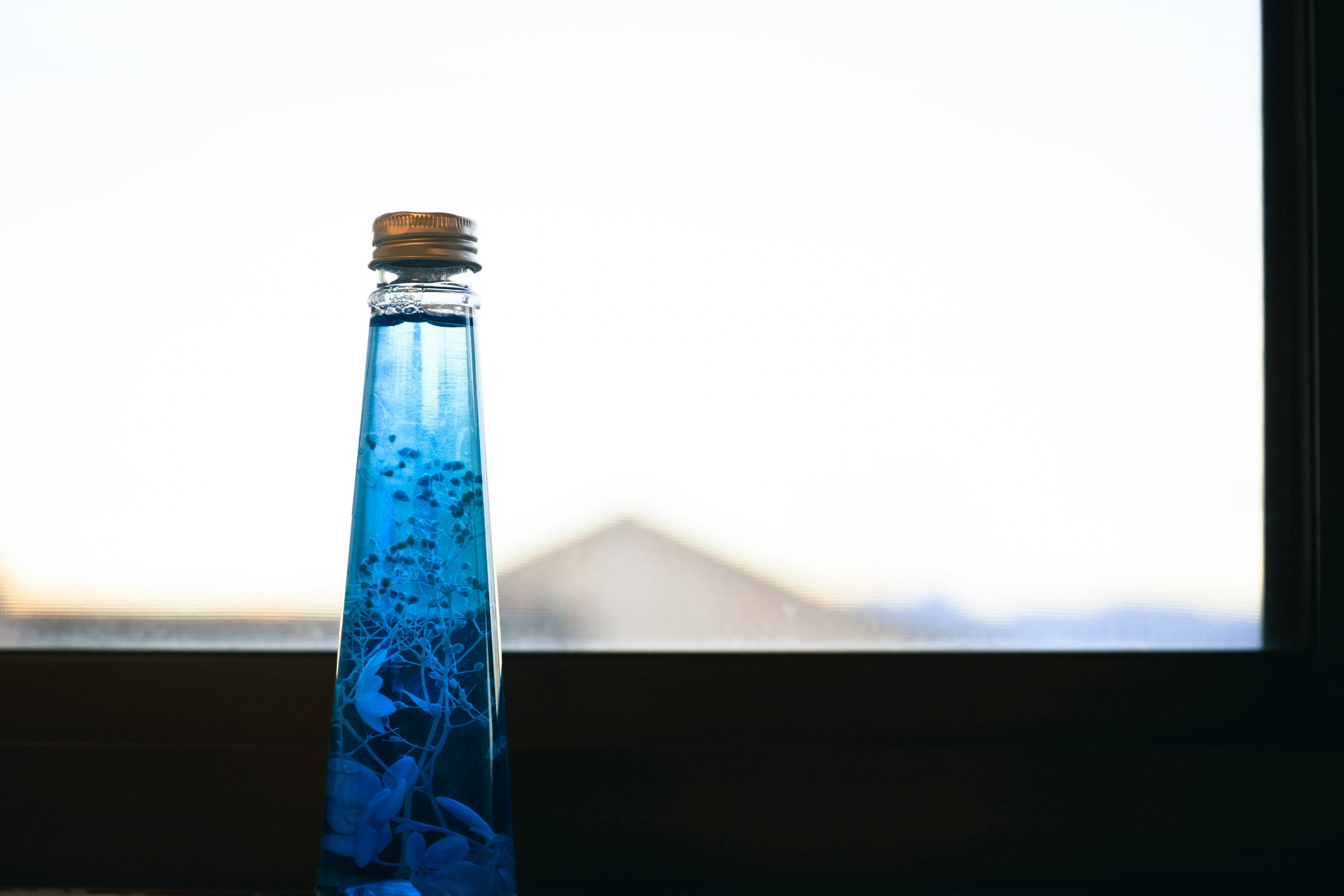 Una botella llena de líquido azul colocada en un alféizar de ventana con un fondo borroso