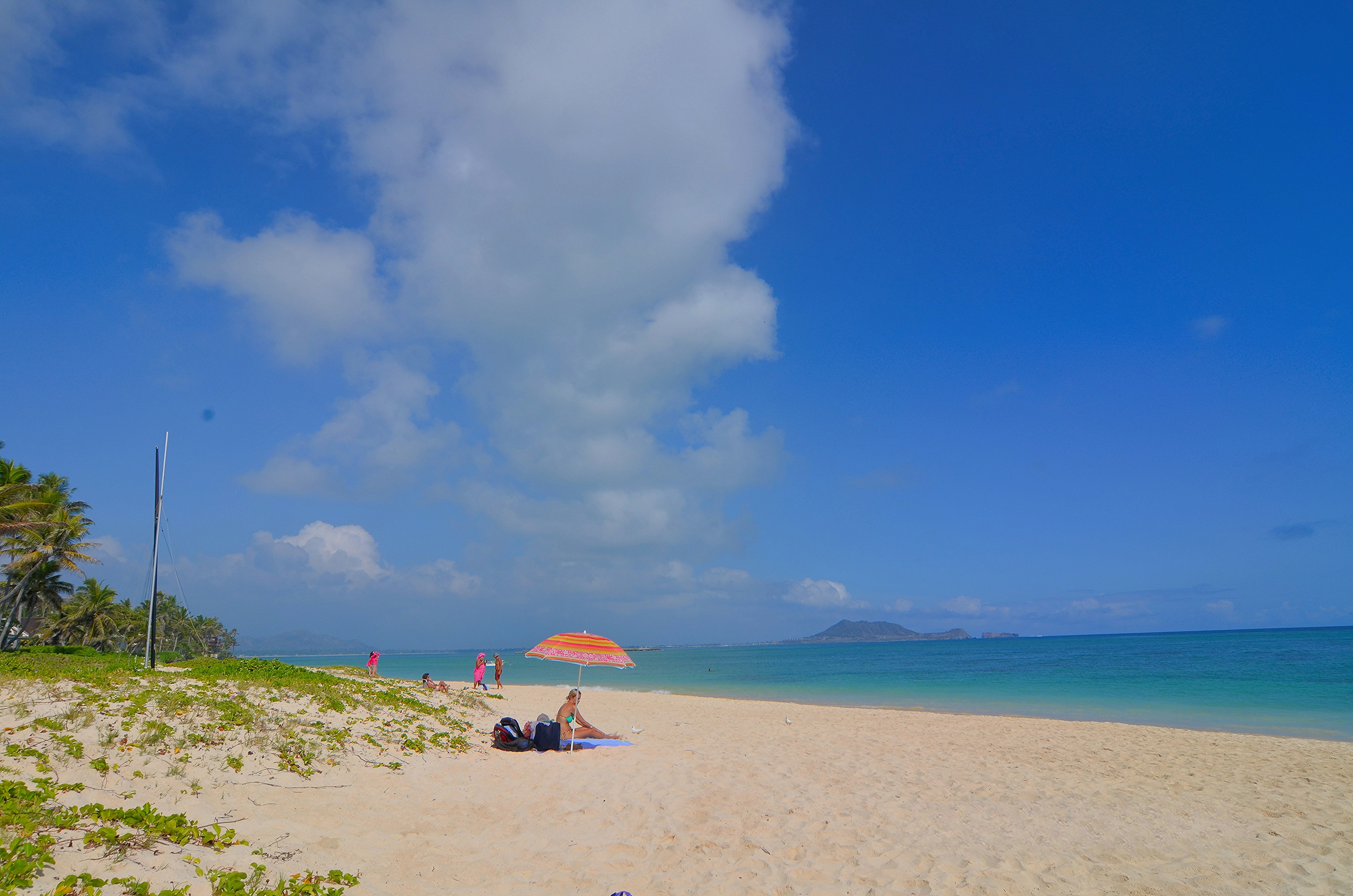 ทิวทัศน์ชายหาดที่มีท้องฟ้าสีฟ้าทรายขาวและผู้คนพักผ่อน