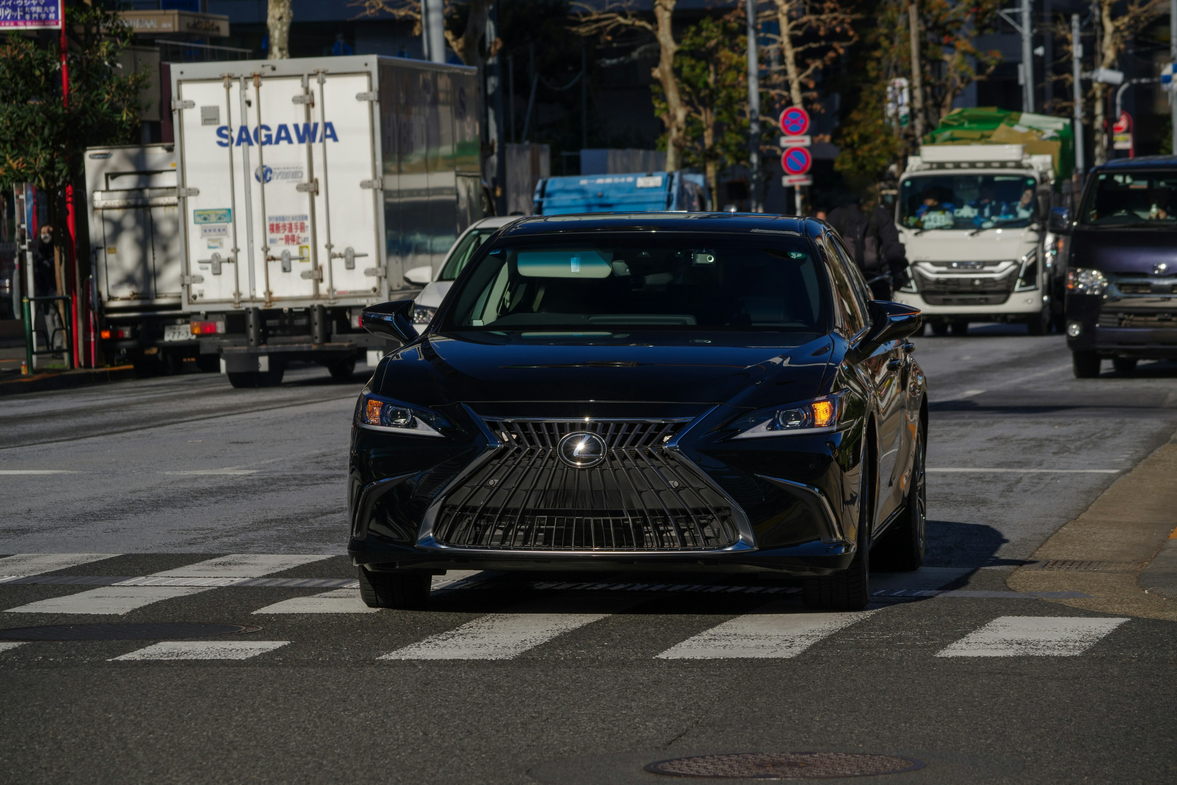 A black Lexus car passing through a crosswalk in an urban setting