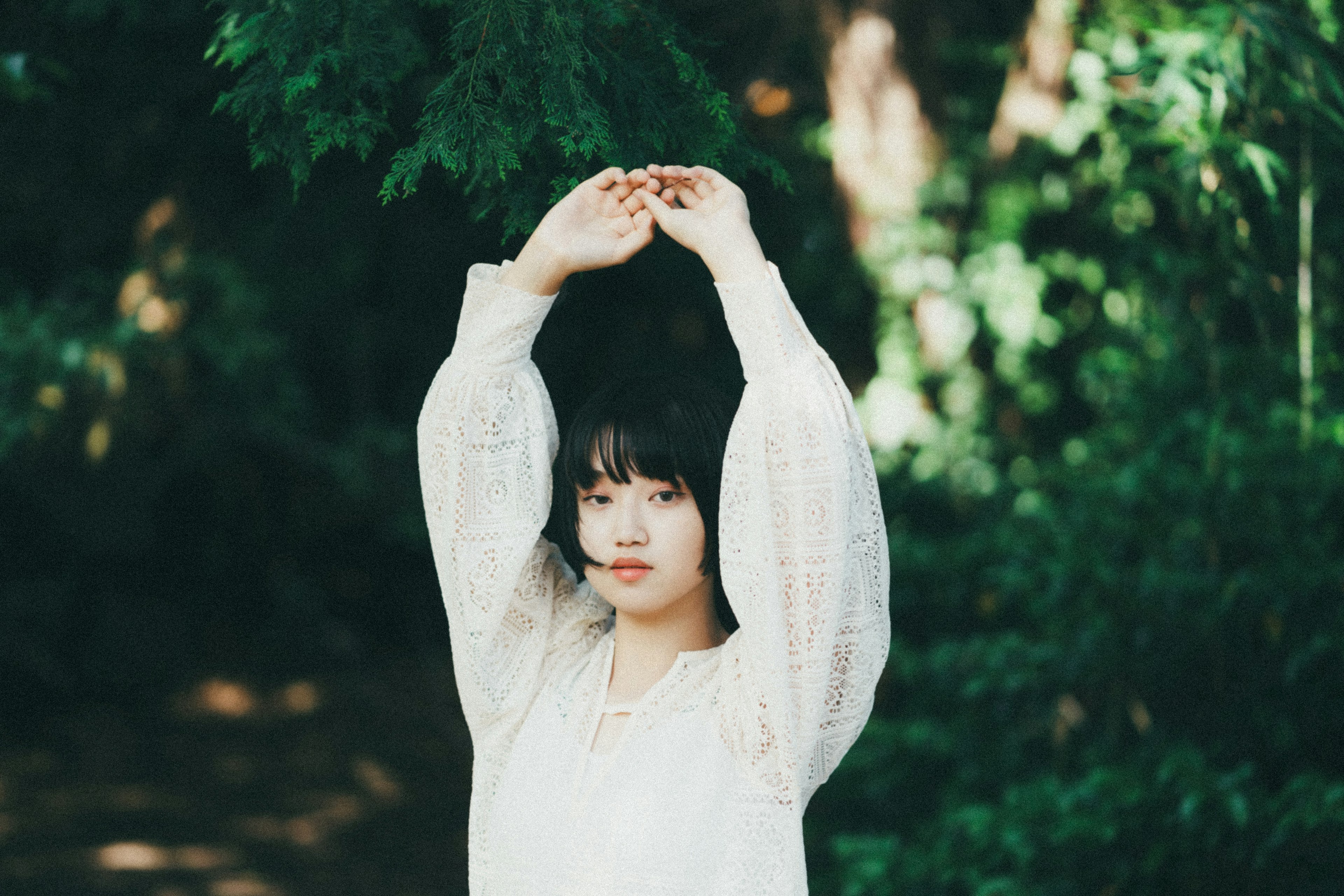 A woman in a white blouse raising her hands against a green background