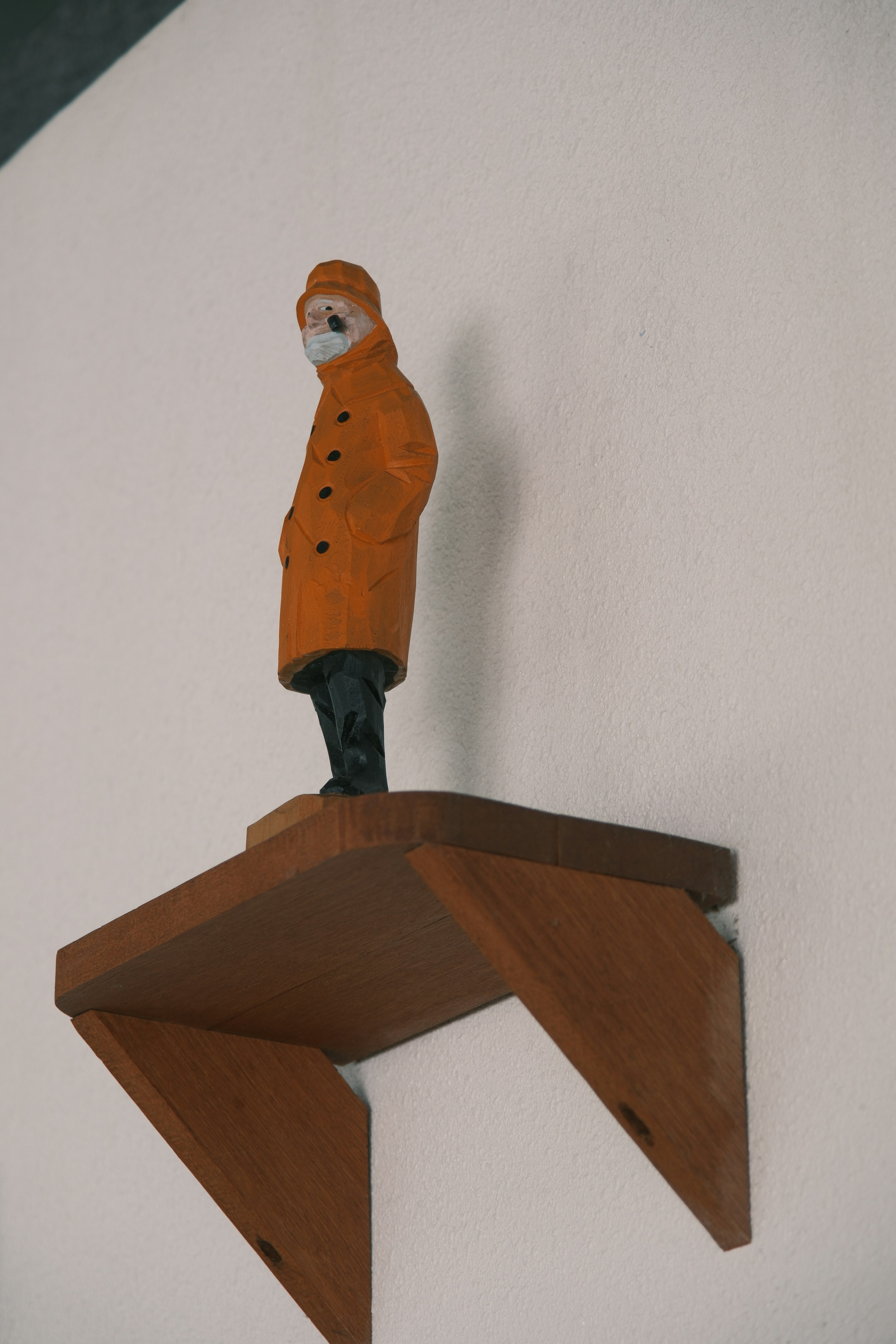 Eine Holzfigur mit einem orangefarbenen Mantel steht auf einem Regal