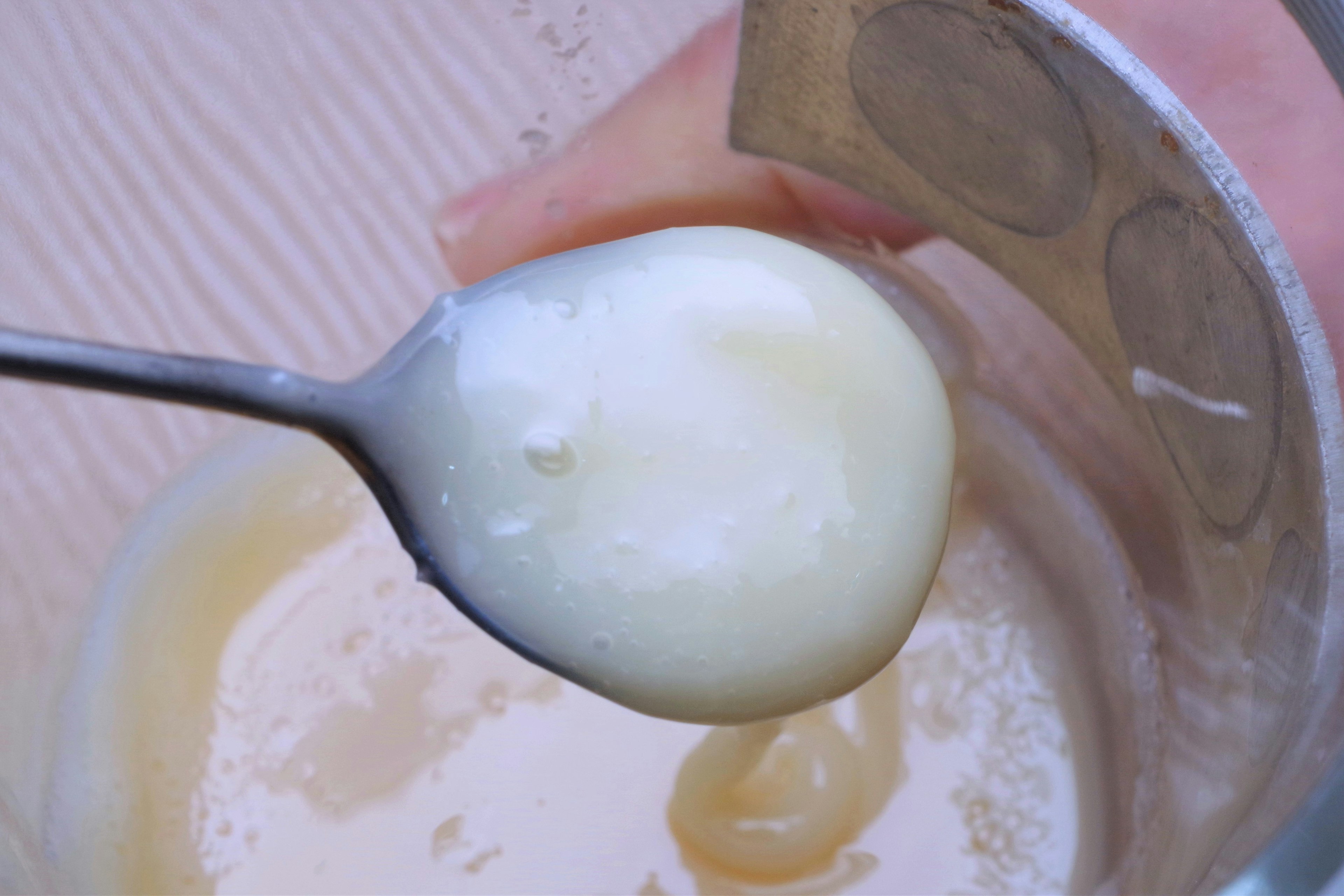 Sustancia blanca cremosa en una cuchara con un recipiente transparente al fondo