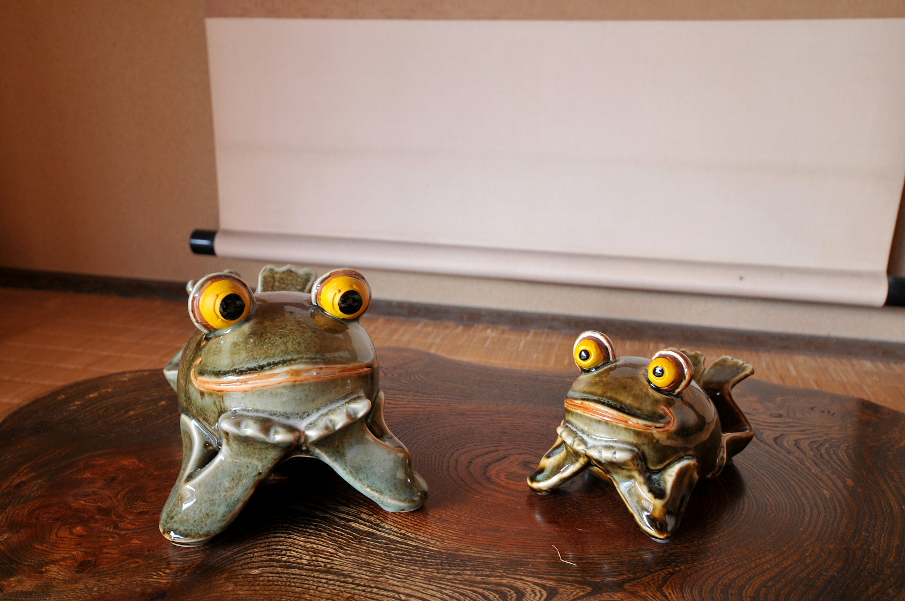 Deux figurines de grenouilles en céramique avec des yeux jaunes sur une surface en bois