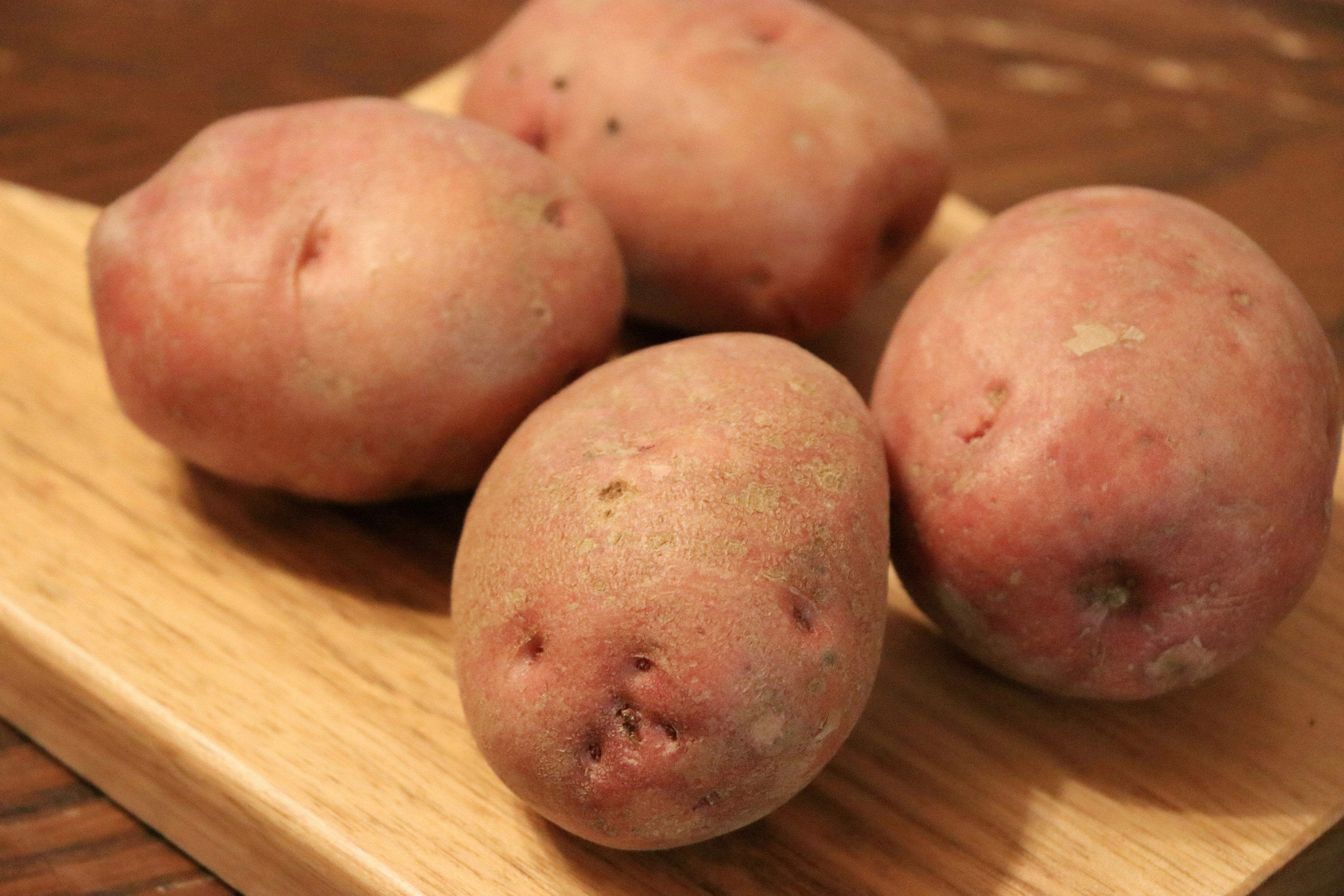 Quatre pommes de terre à peau rouge sur une planche en bois