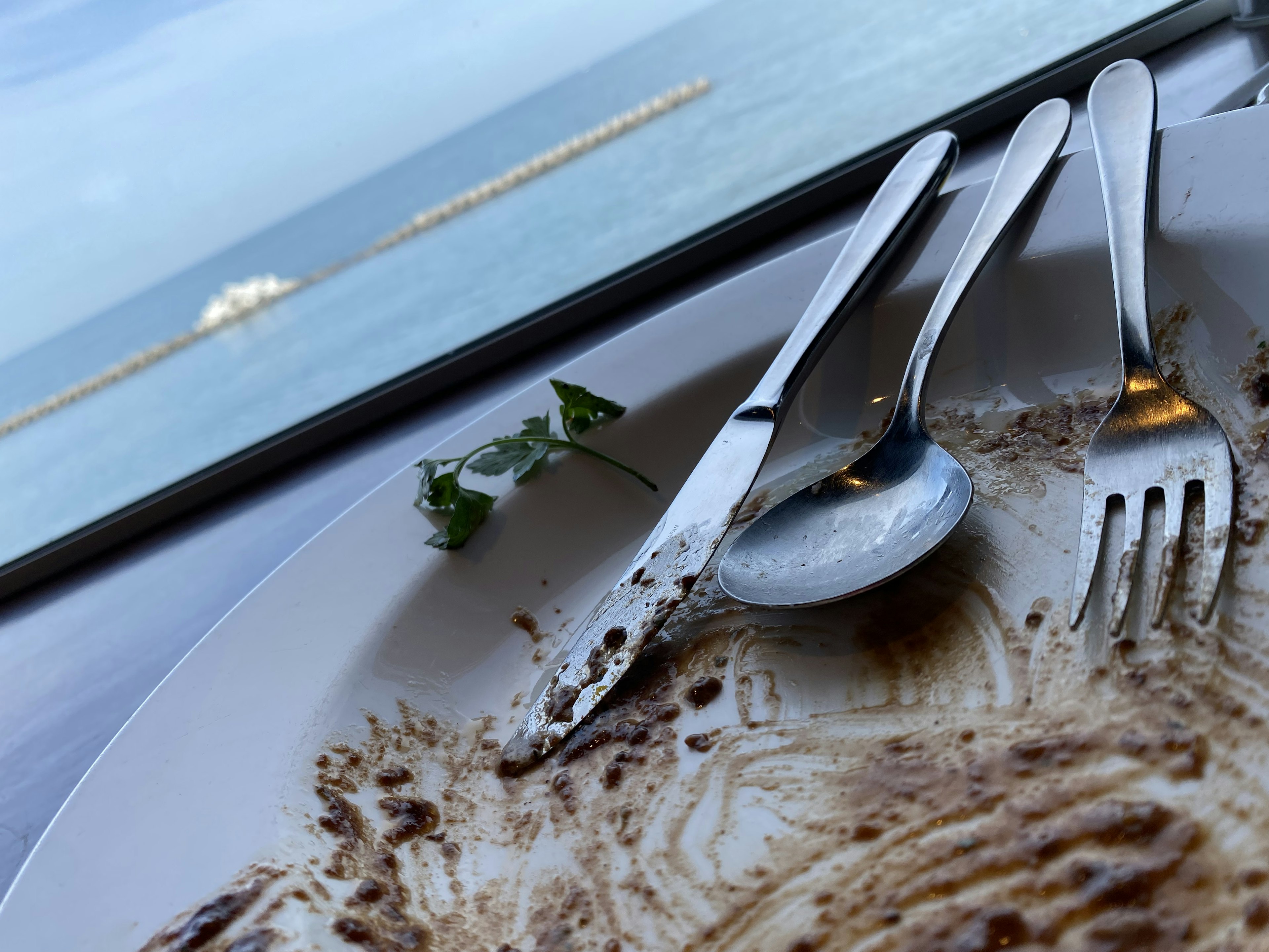 皿に残った食べかすの上に置かれたナイフとフォークとスプーン 残りの食べ物の跡が見える