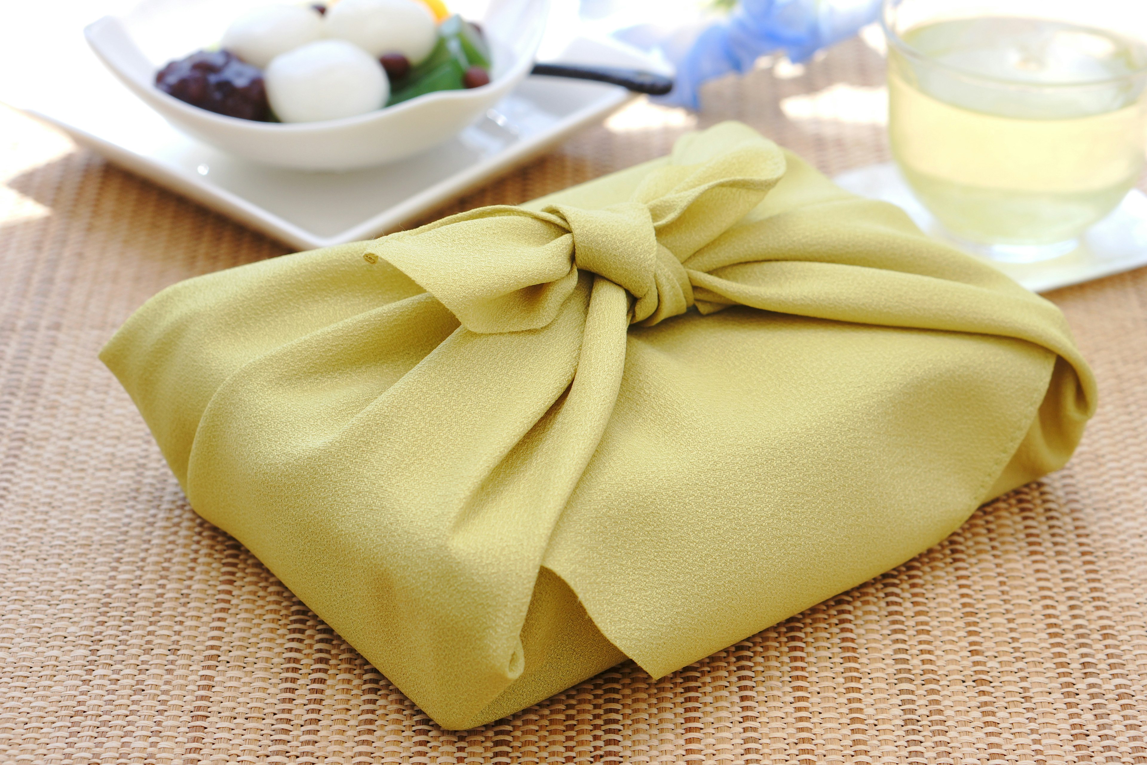 A yellow fabric-wrapped food gift box with a plate of dessert and tea in the background