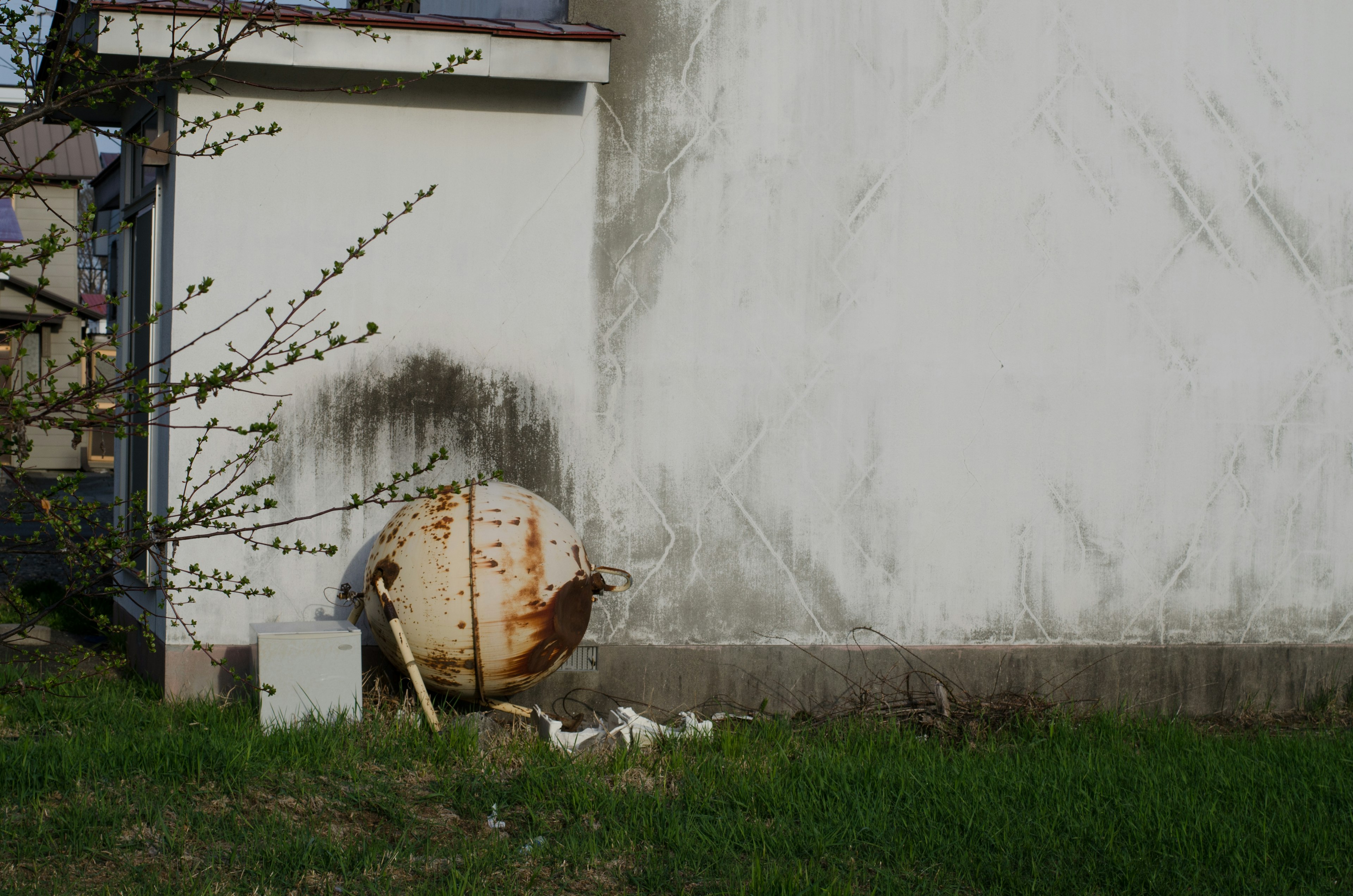 Contenedor redondo oxidado al lado de una pared blanca con hierba verde alrededor