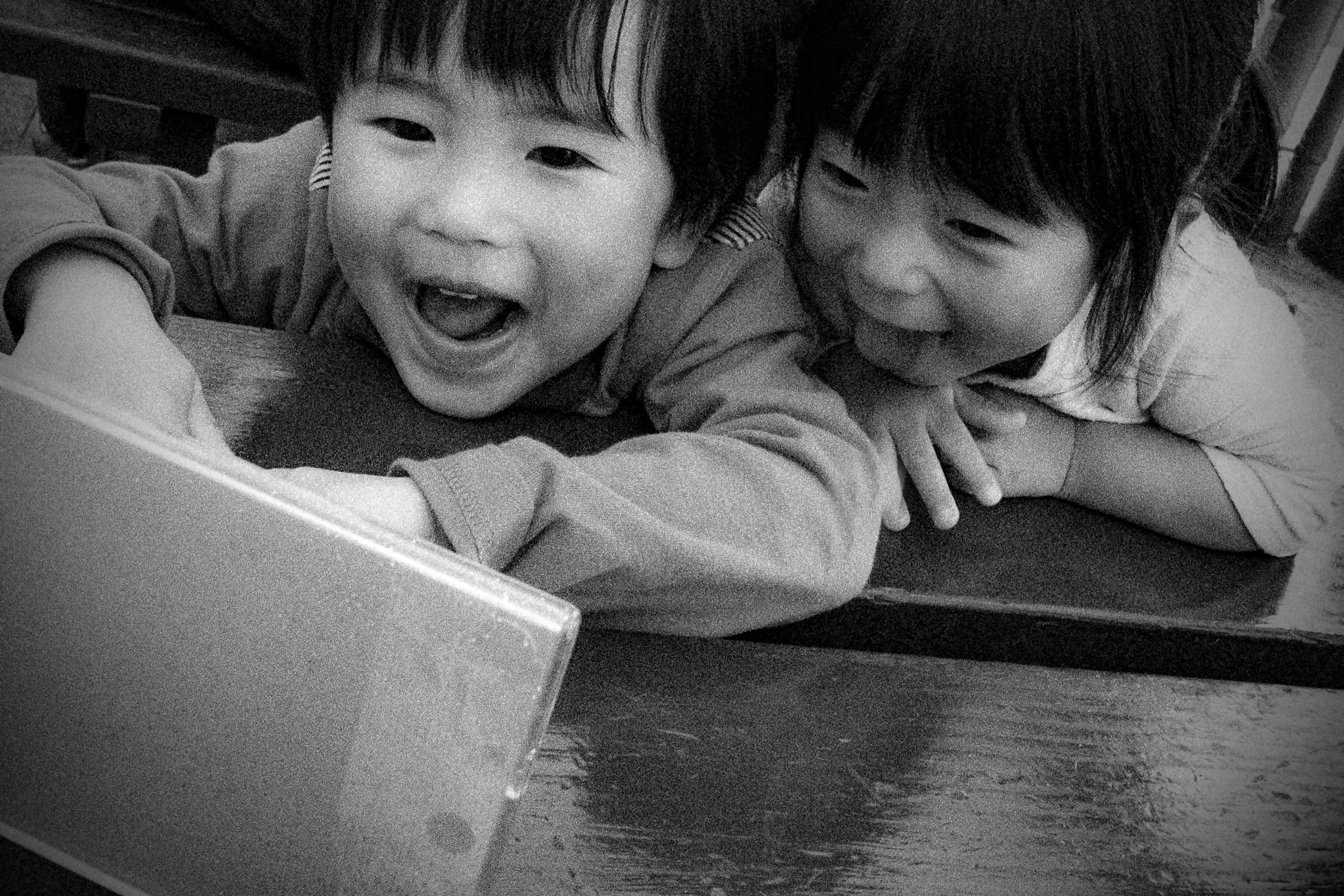 Deux enfants souriants regardant un écran dans une image en noir et blanc