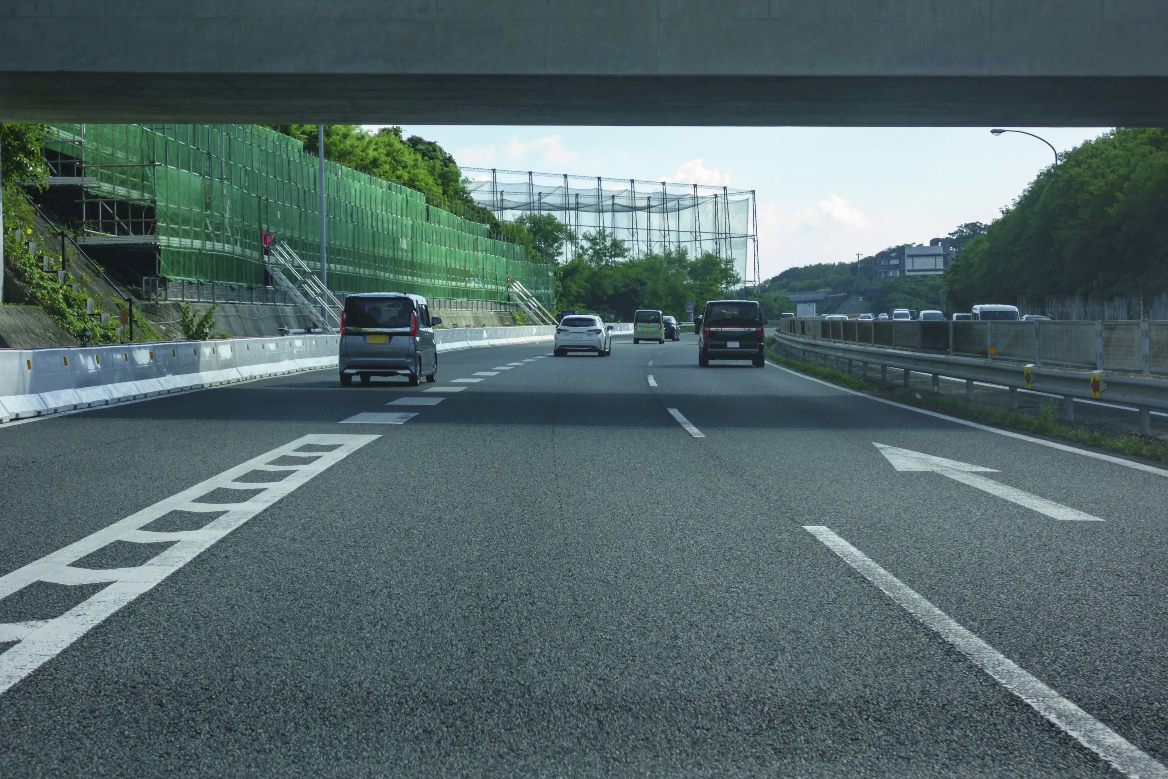 View of a highway under an overpass vehicles in motion green scenery in the background