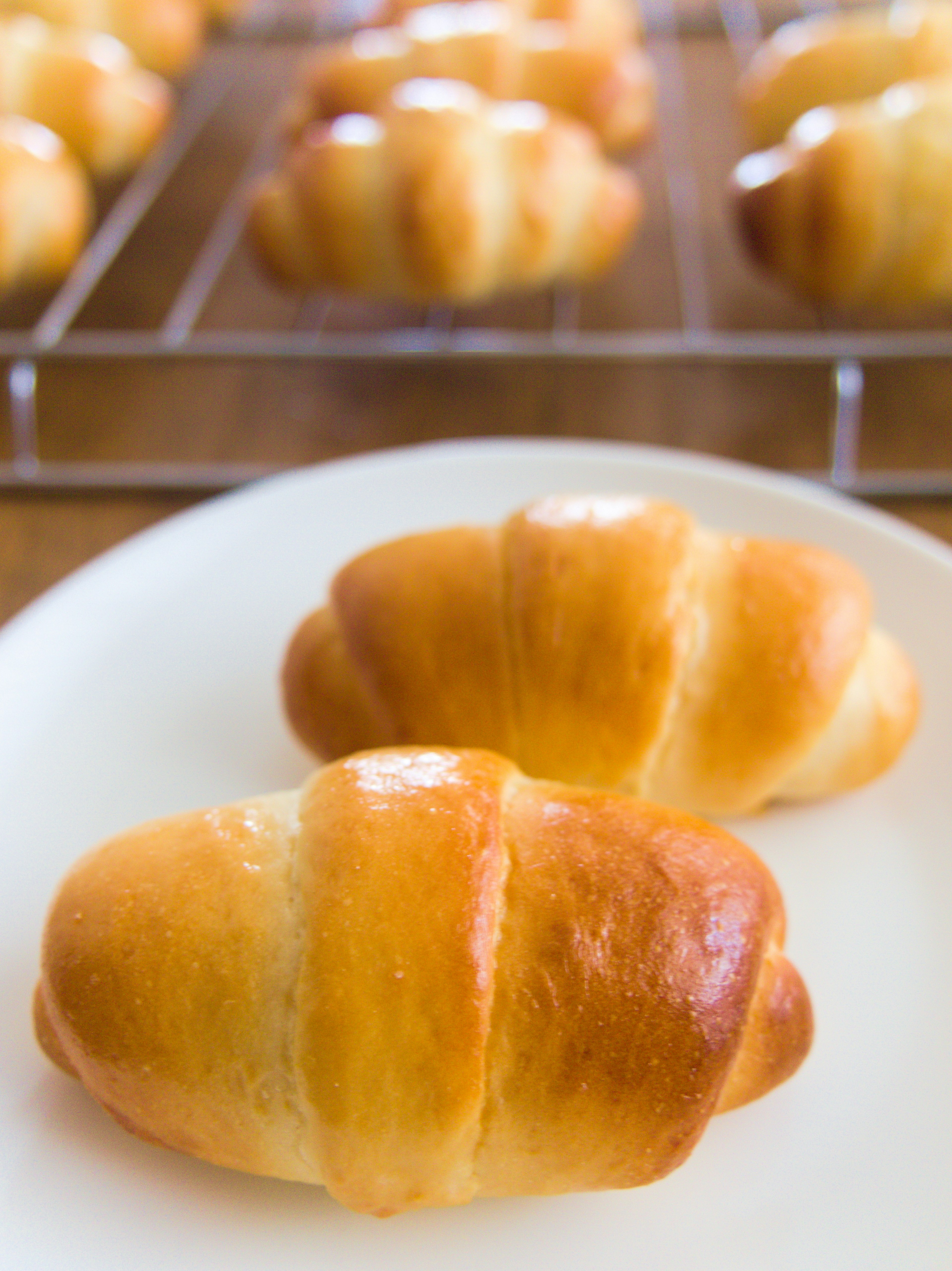 Croissants recién horneados en un plato con otros croissants en una rejilla de enfriamiento al fondo