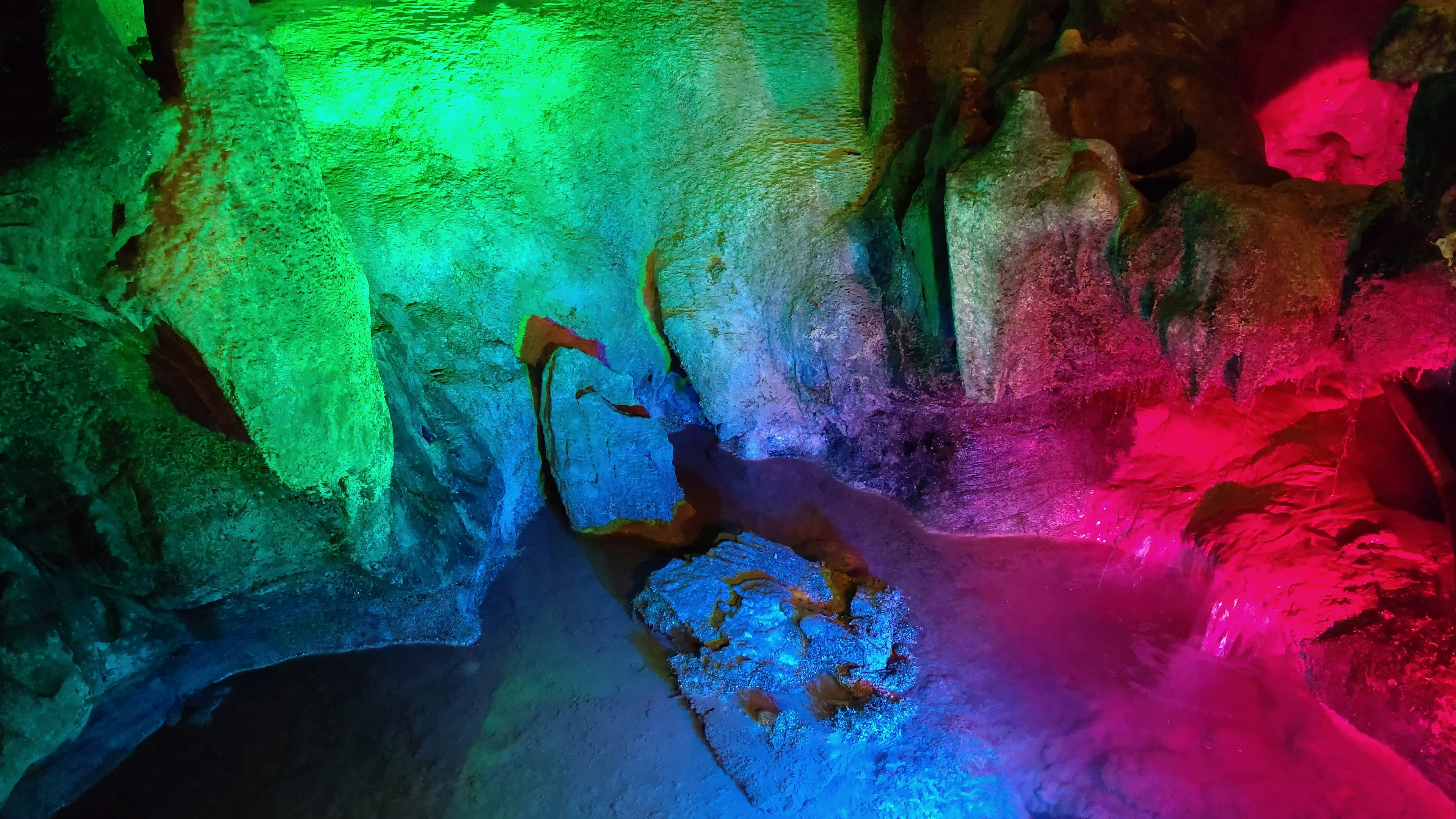 Intérieur d'une grotte illuminée par des lumières colorées en vert, bleu et rose