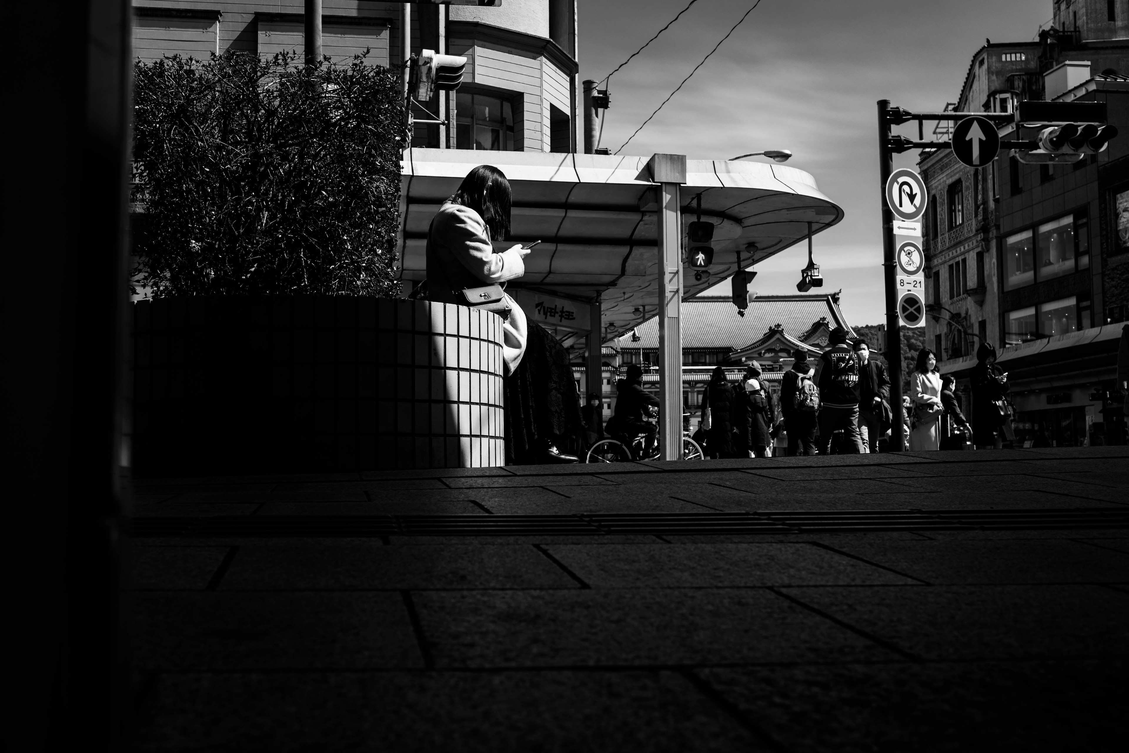 Une personne assise sur un banc dans un paysage urbain fort contraste en noir et blanc