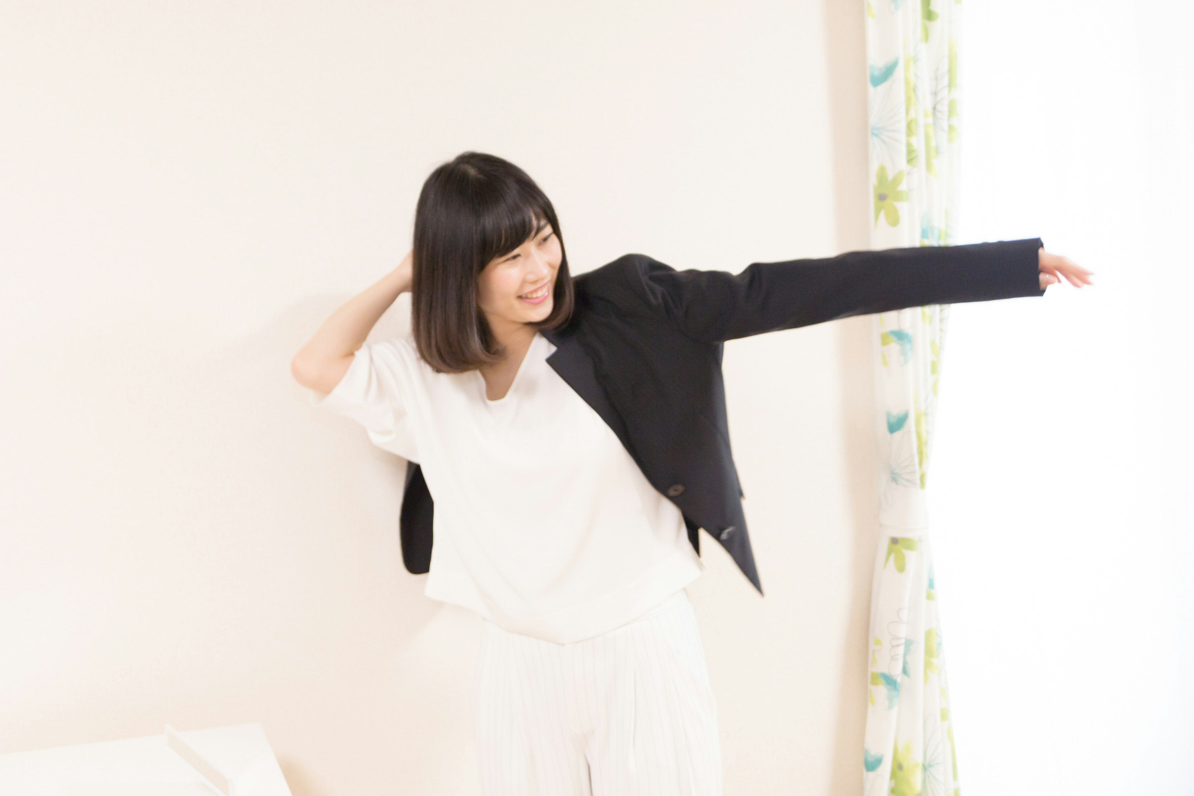 A woman in a white outfit wearing a black jacket stretching her arm