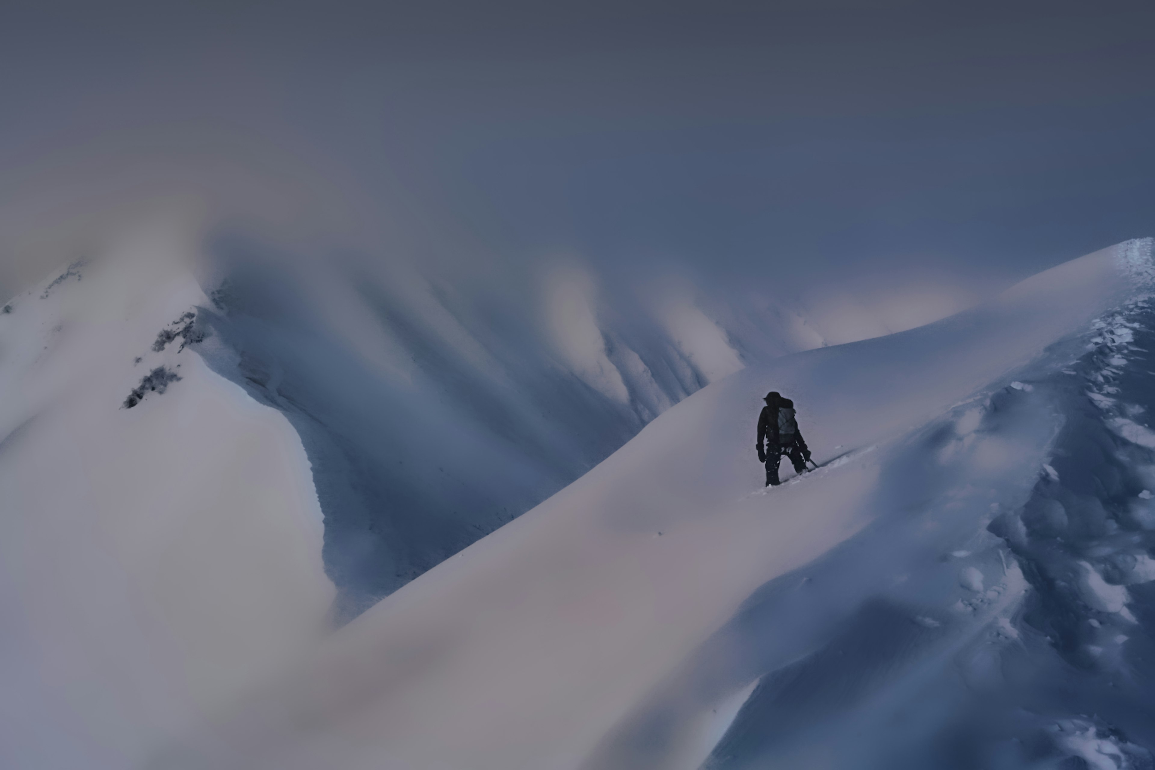 Silhouette of a climber walking on a snow-covered mountain ridge