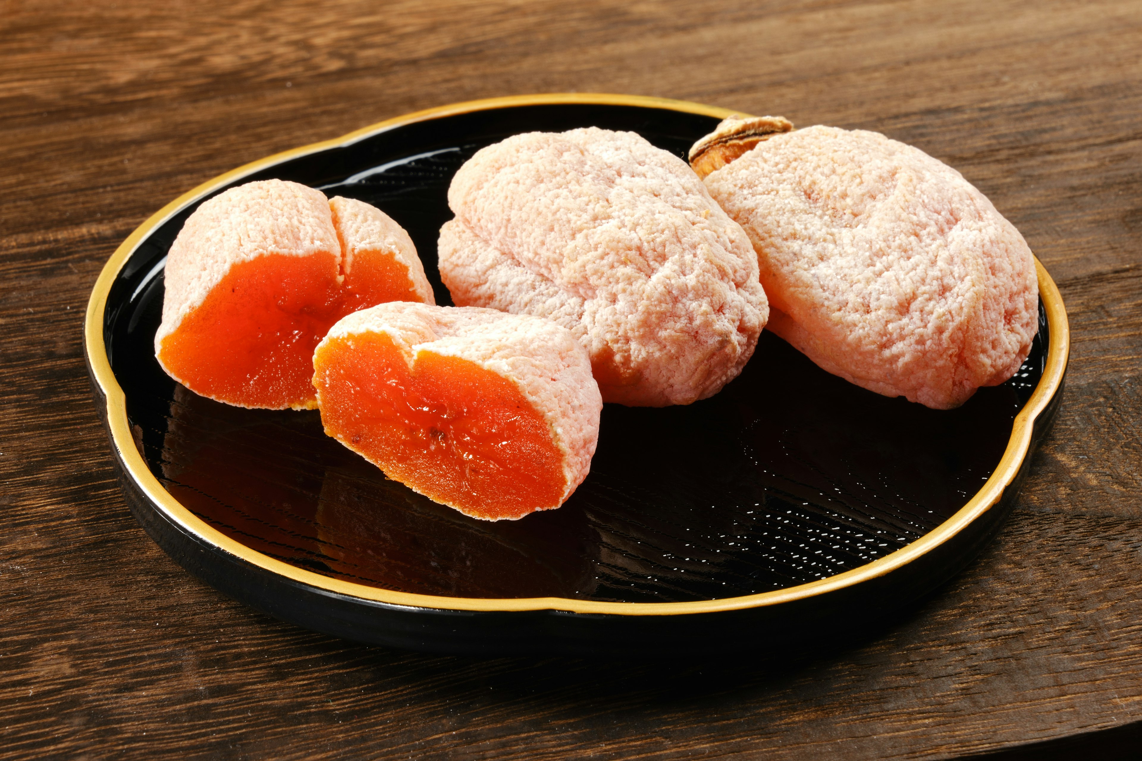 Mochi naranja suave en un plato negro con un trozo cortado que muestra el relleno