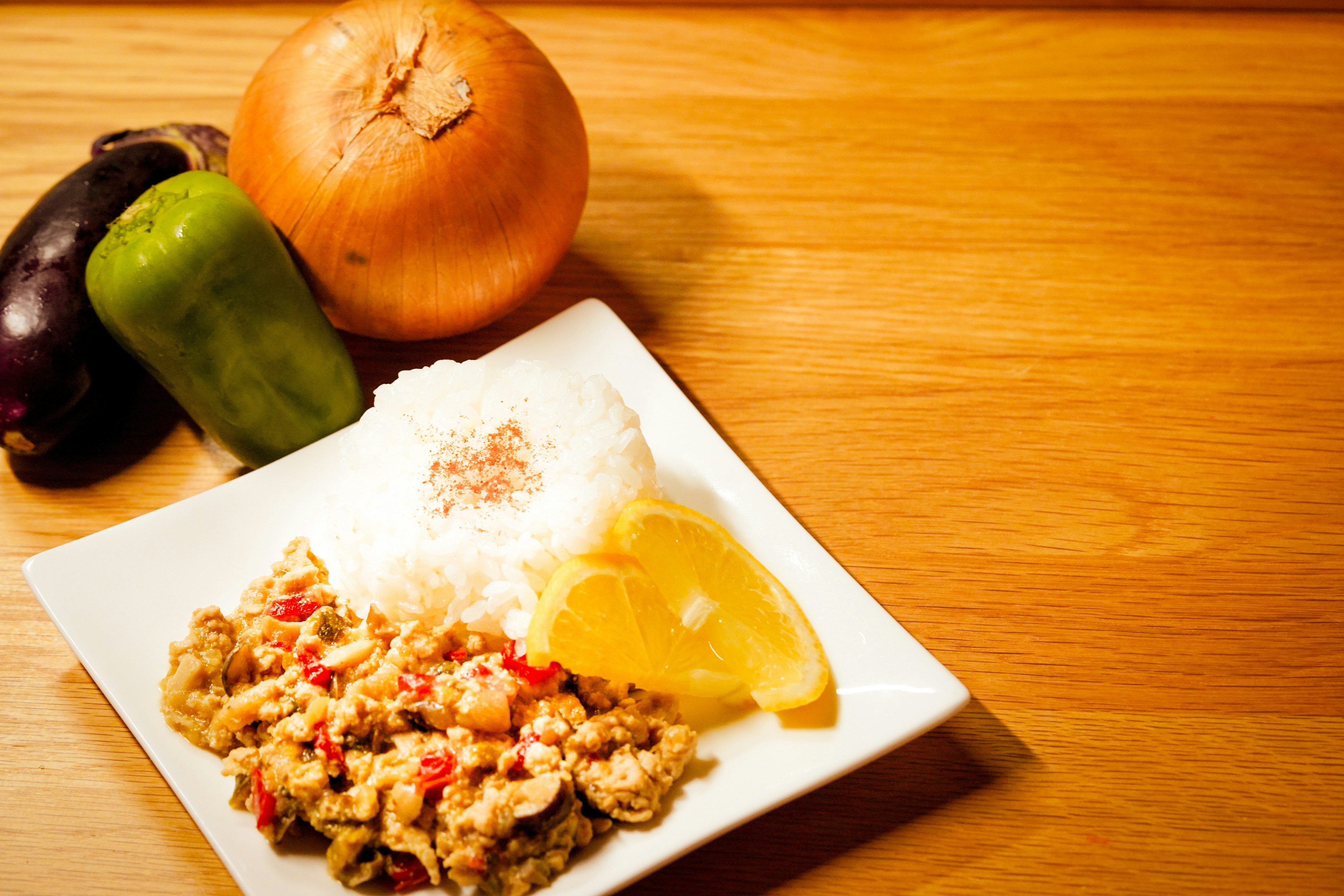 Hidangan nasi dan telur orak-arik di piring putih dengan paprika hijau dan bawang di latar belakang di atas meja kayu