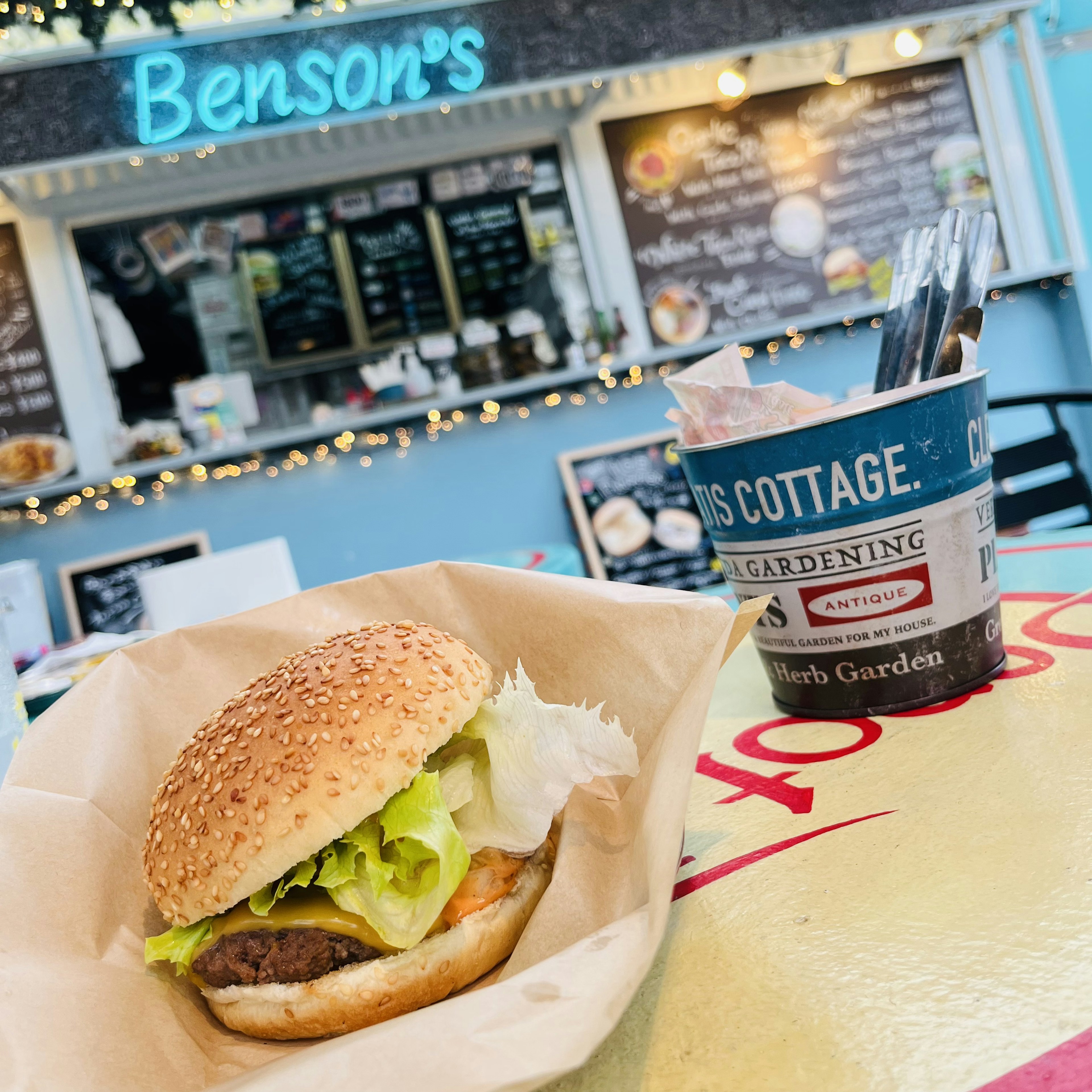 A hamburger from Benson's with lettuce on a table next to a drink