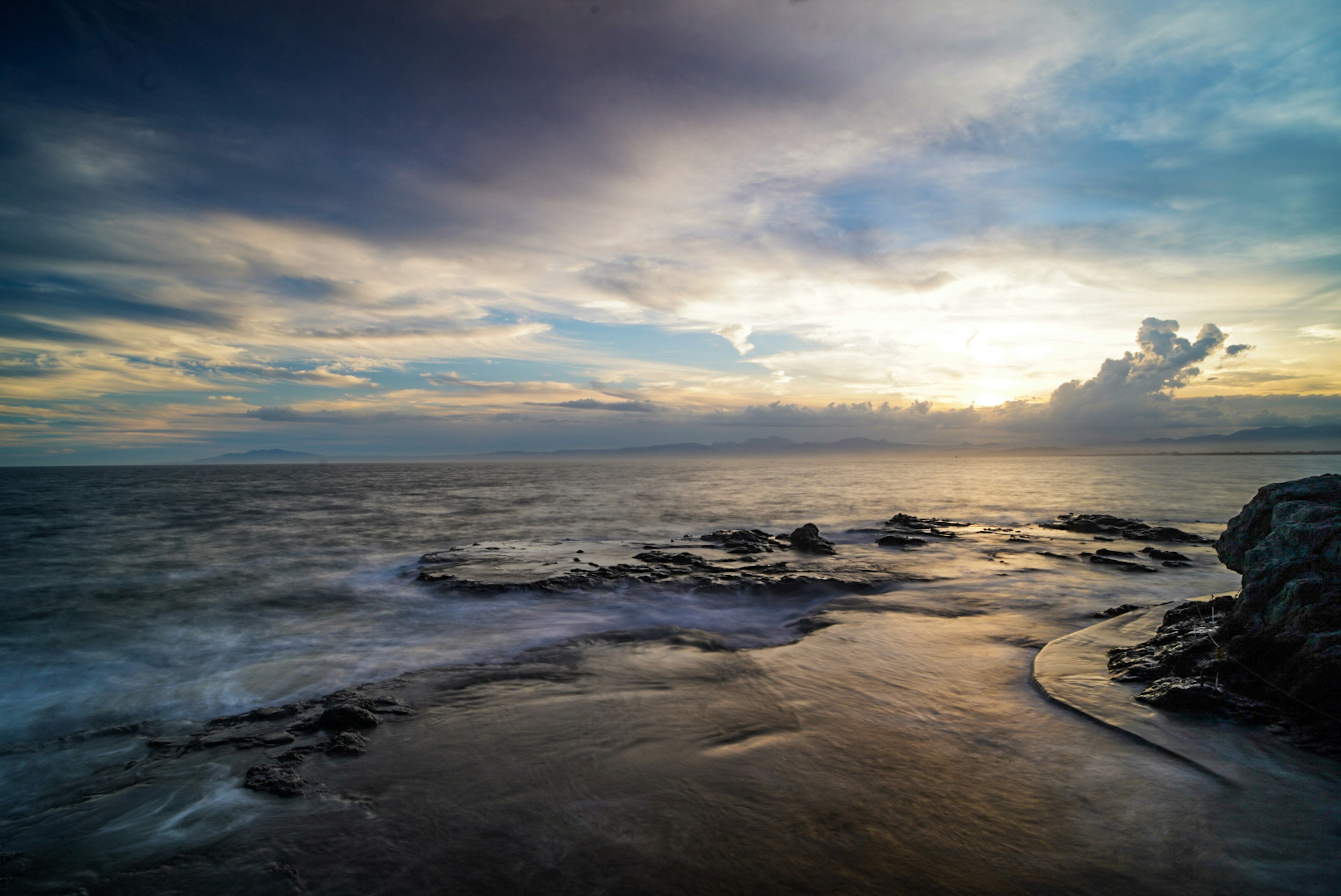 美しい海の風景と夕日が雲の間から見える