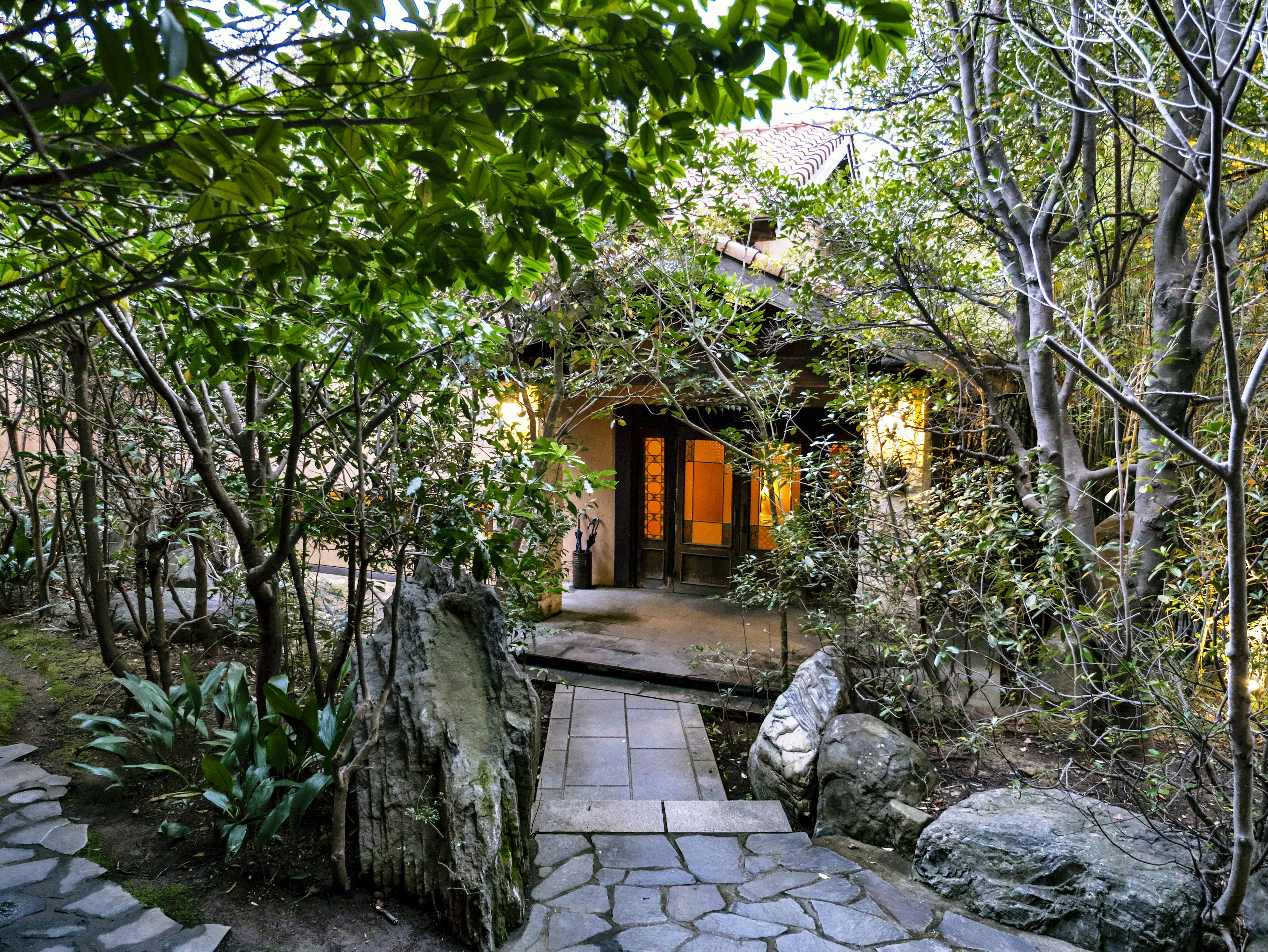 Entrée d'une maison entourée de verdure luxuriante et de pierres