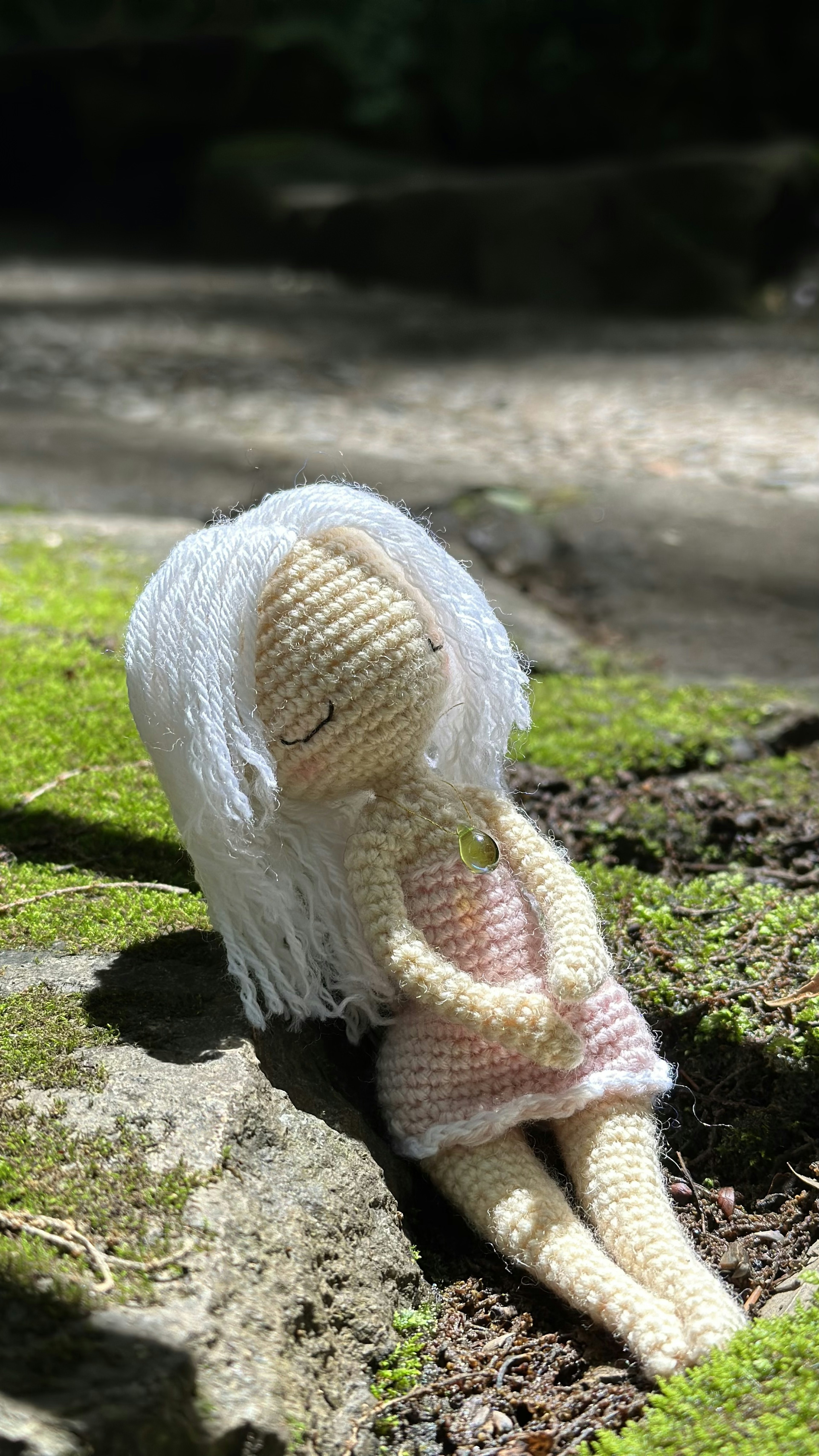 Crocheted doll with white hair sitting on green moss