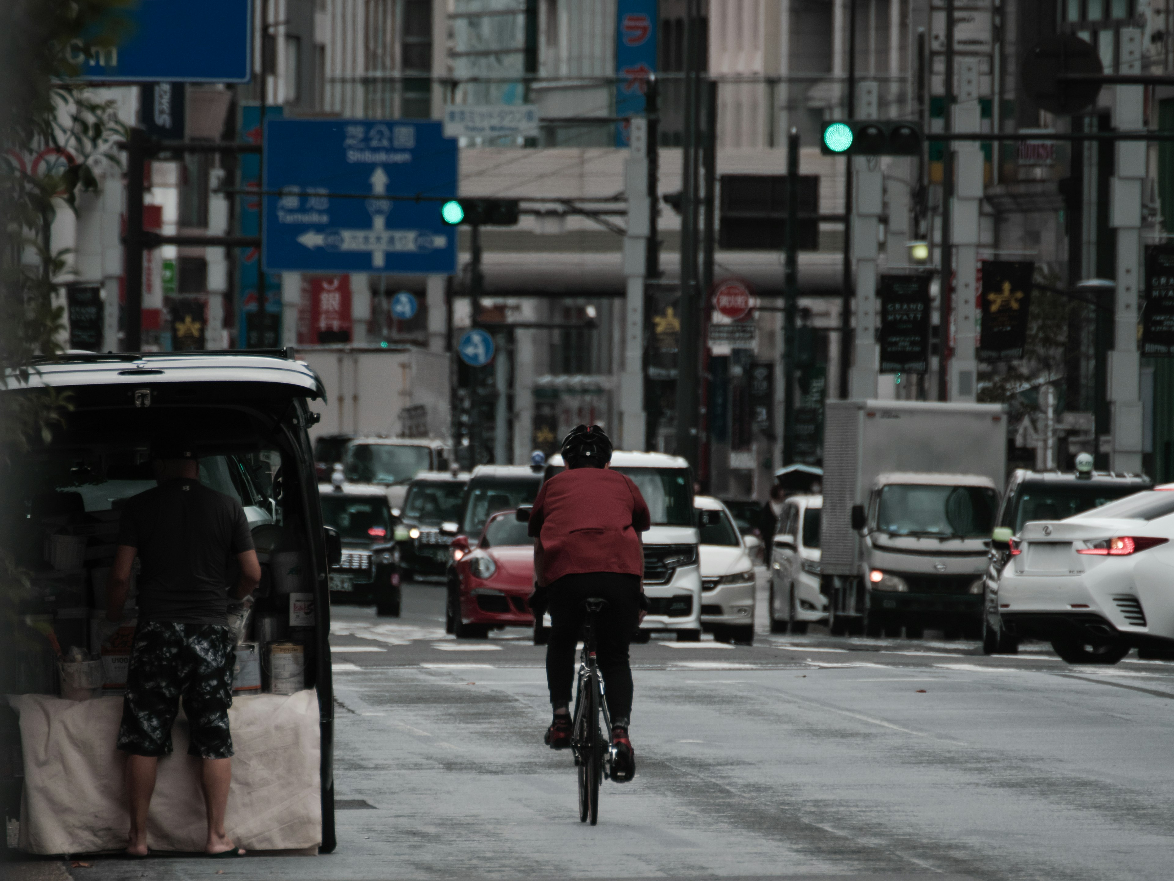 Eine Person fährt mit dem Fahrrad auf einer Stadtstraße mit grünen Ampeln und vorbeifahrenden Fahrzeugen