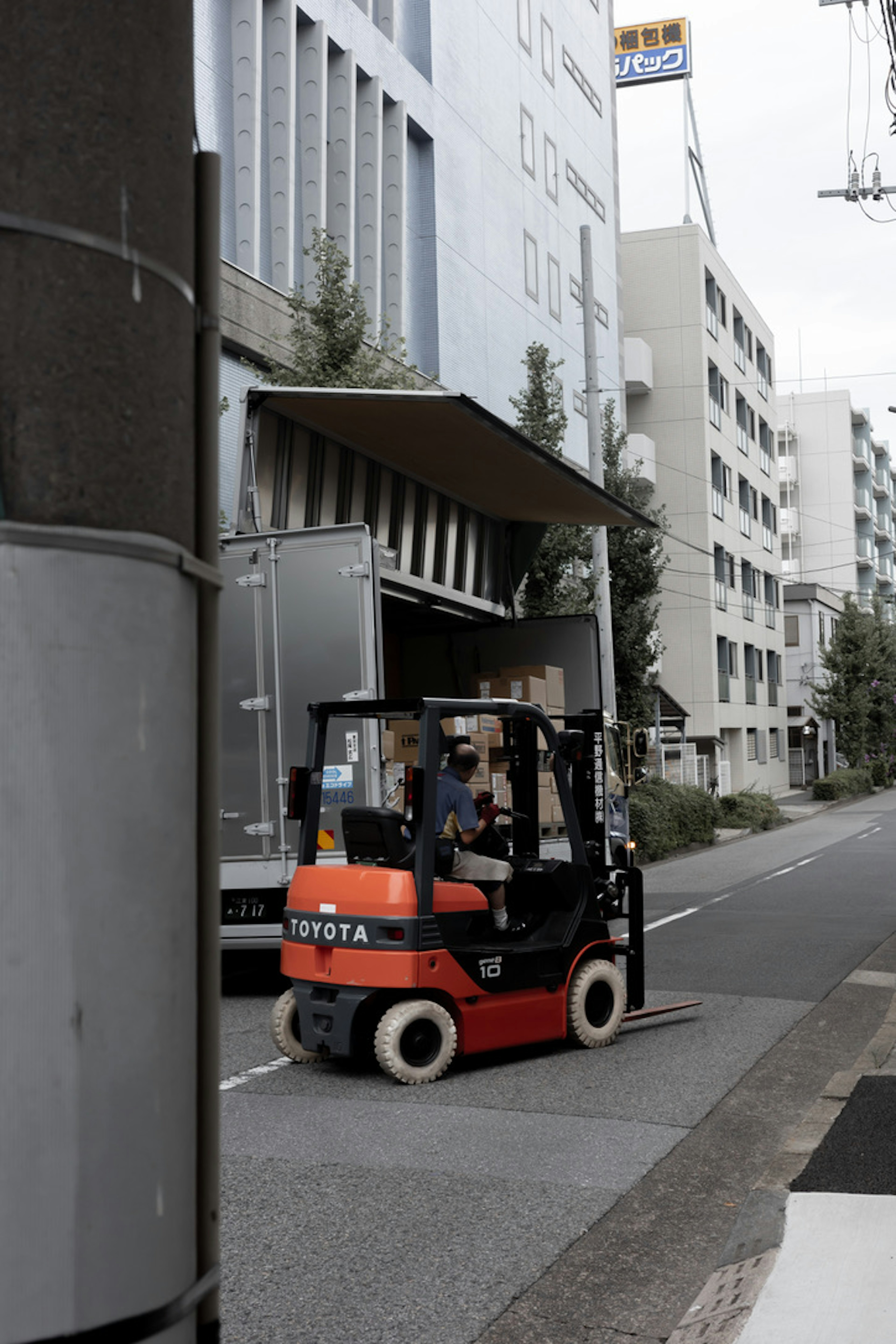 フォークリフトが街中の建物の前で荷物を運んでいる様子