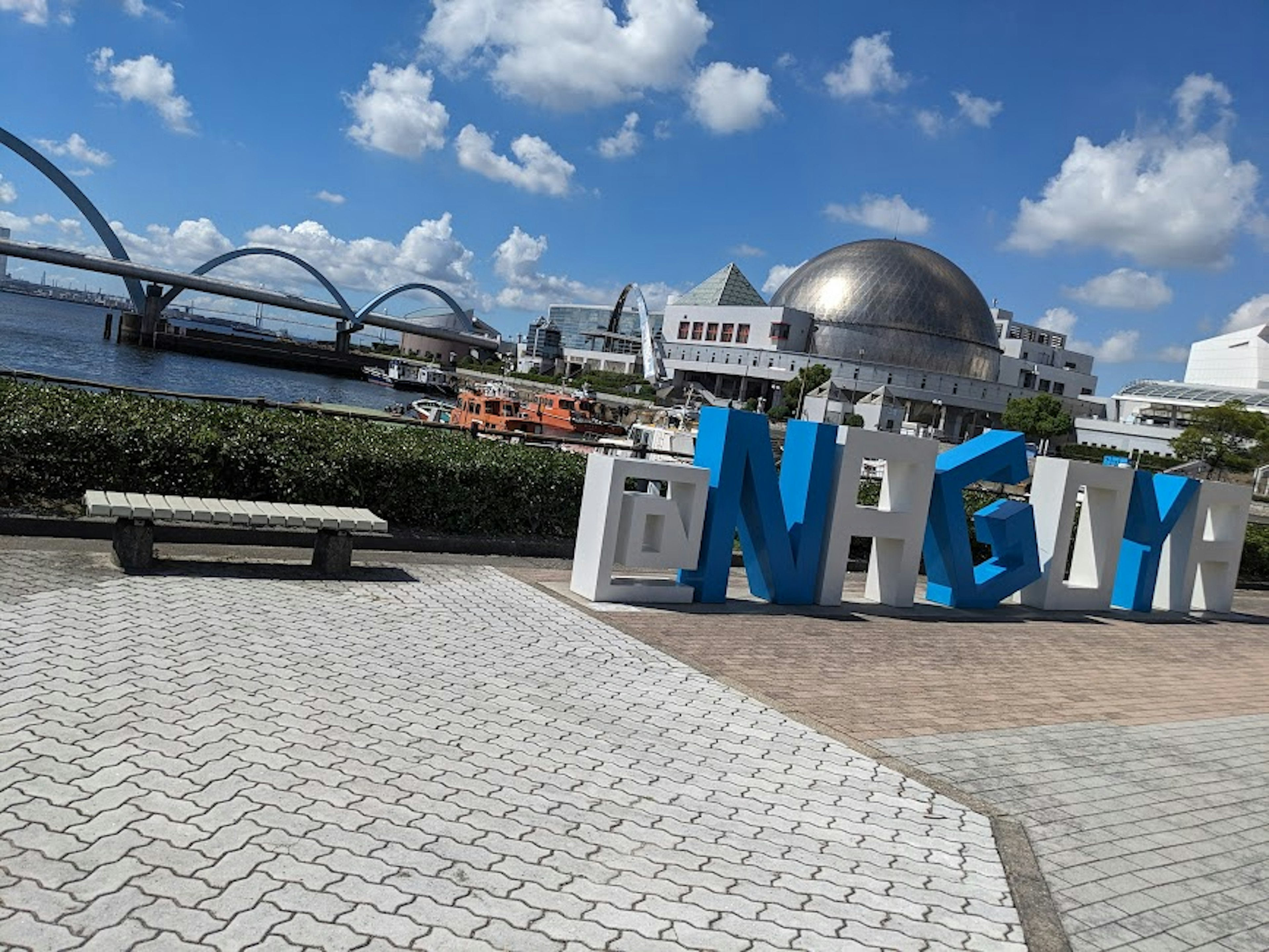 Large blue letters spelling 'NEW' with a waterfront view and modern architecture