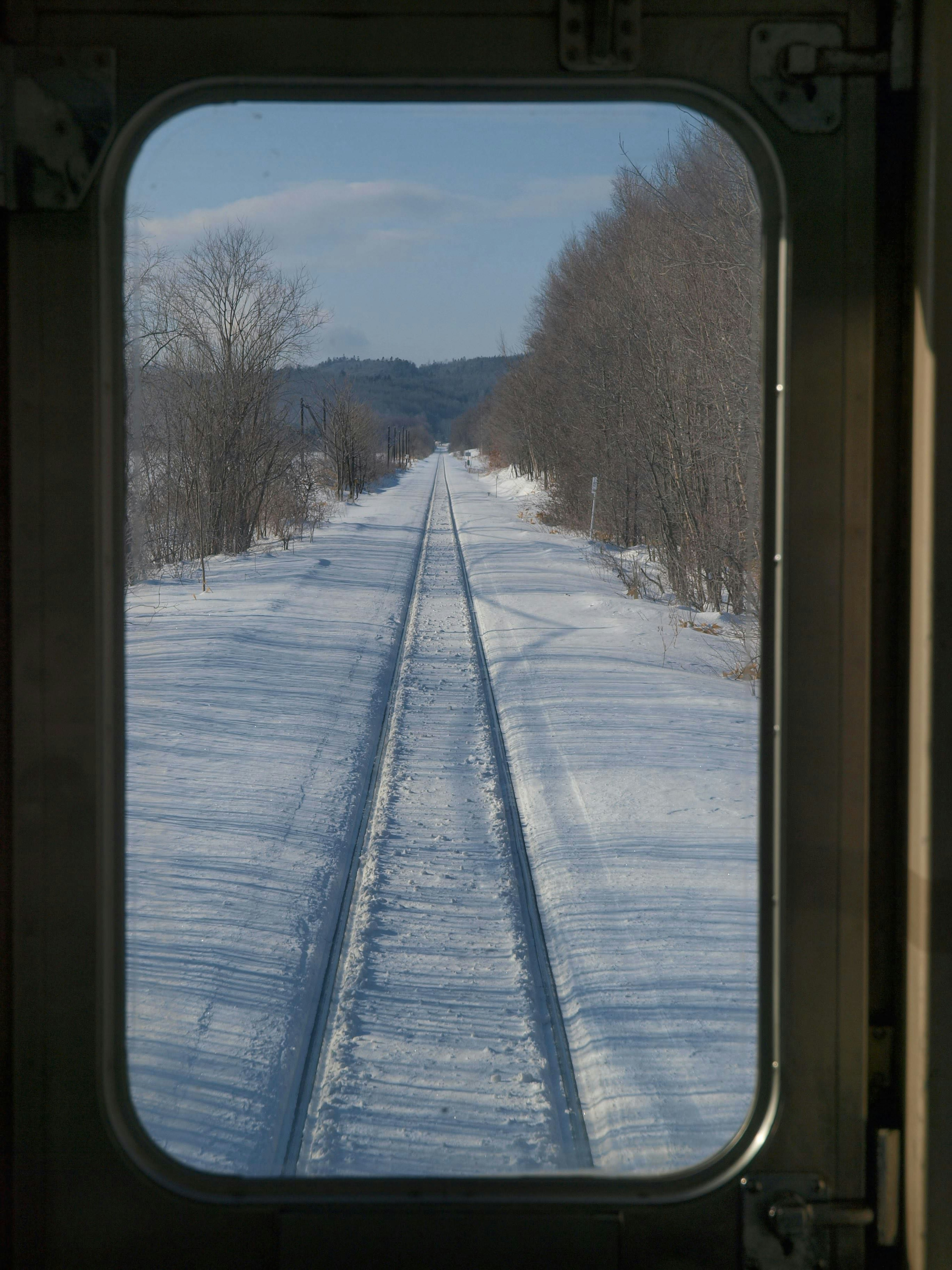 วิวของรางรถไฟที่ปกคลุมด้วยหิมะผ่านหน้าต่างรถไฟ