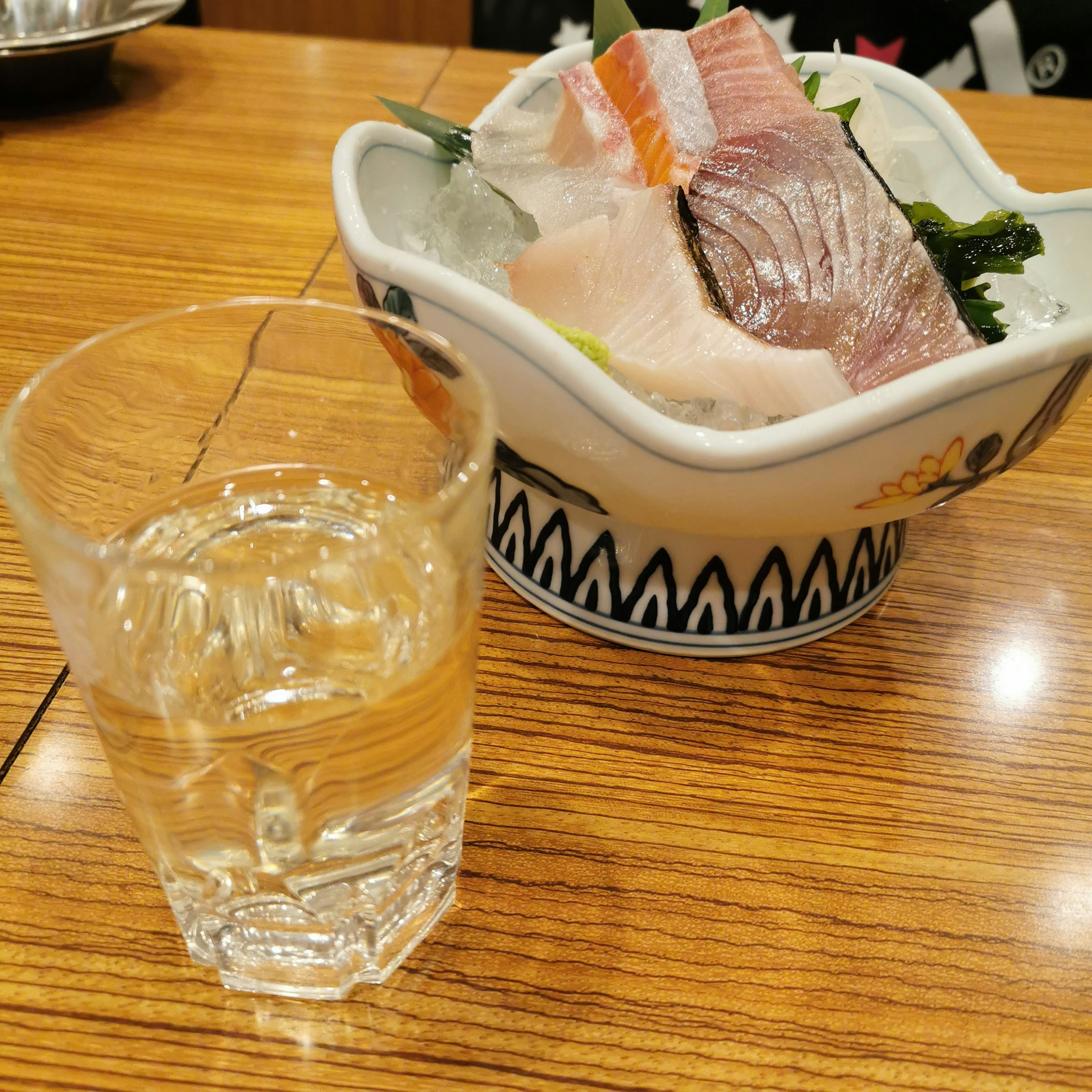 Sashimi fresco y un vaso de sake sobre una mesa de madera