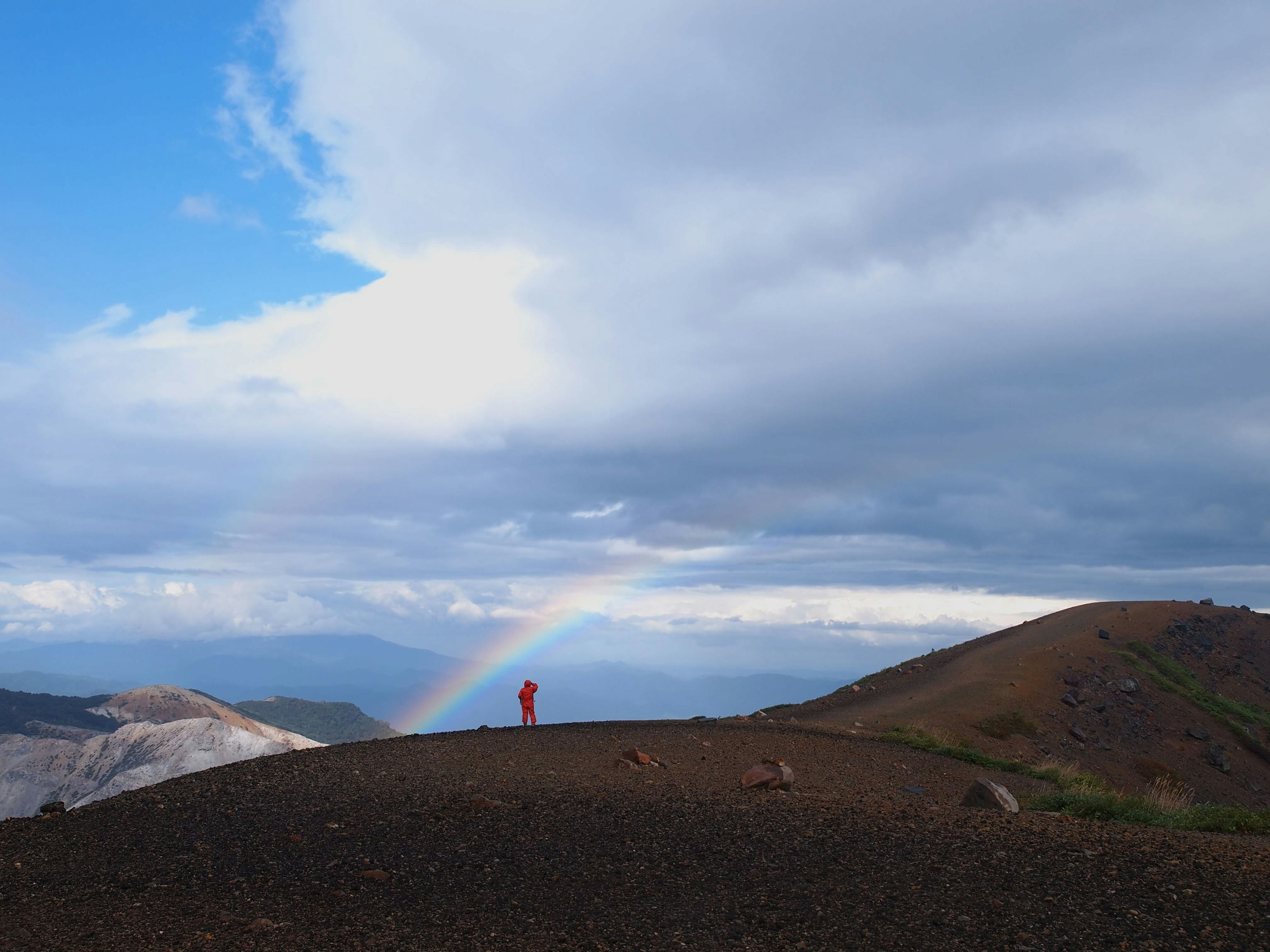 Persona de pie en una cresta montañosa con un arco iris de fondo