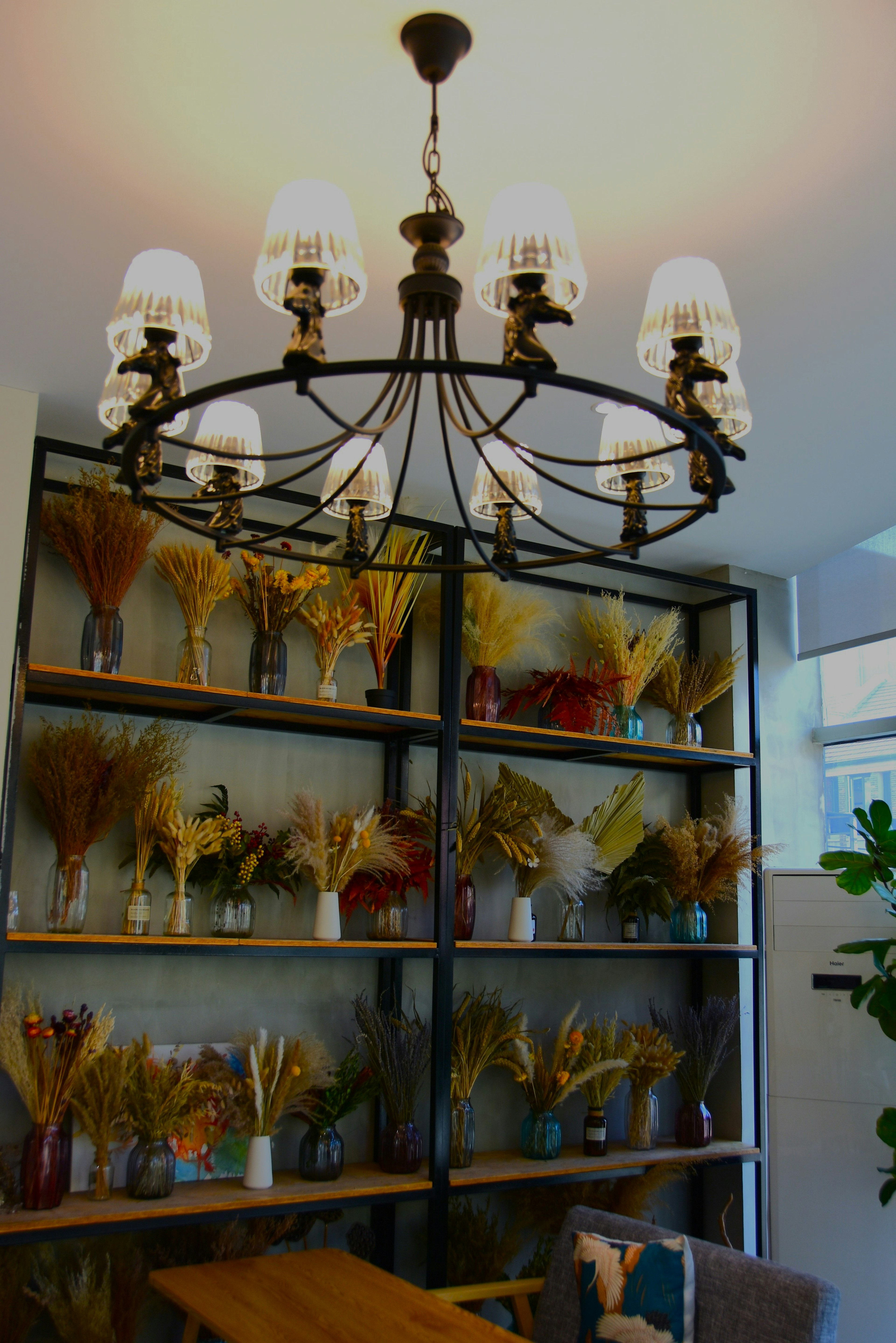 Modern interior room with a chandelier overhead featuring a shelf of dried flowers in vases in the background