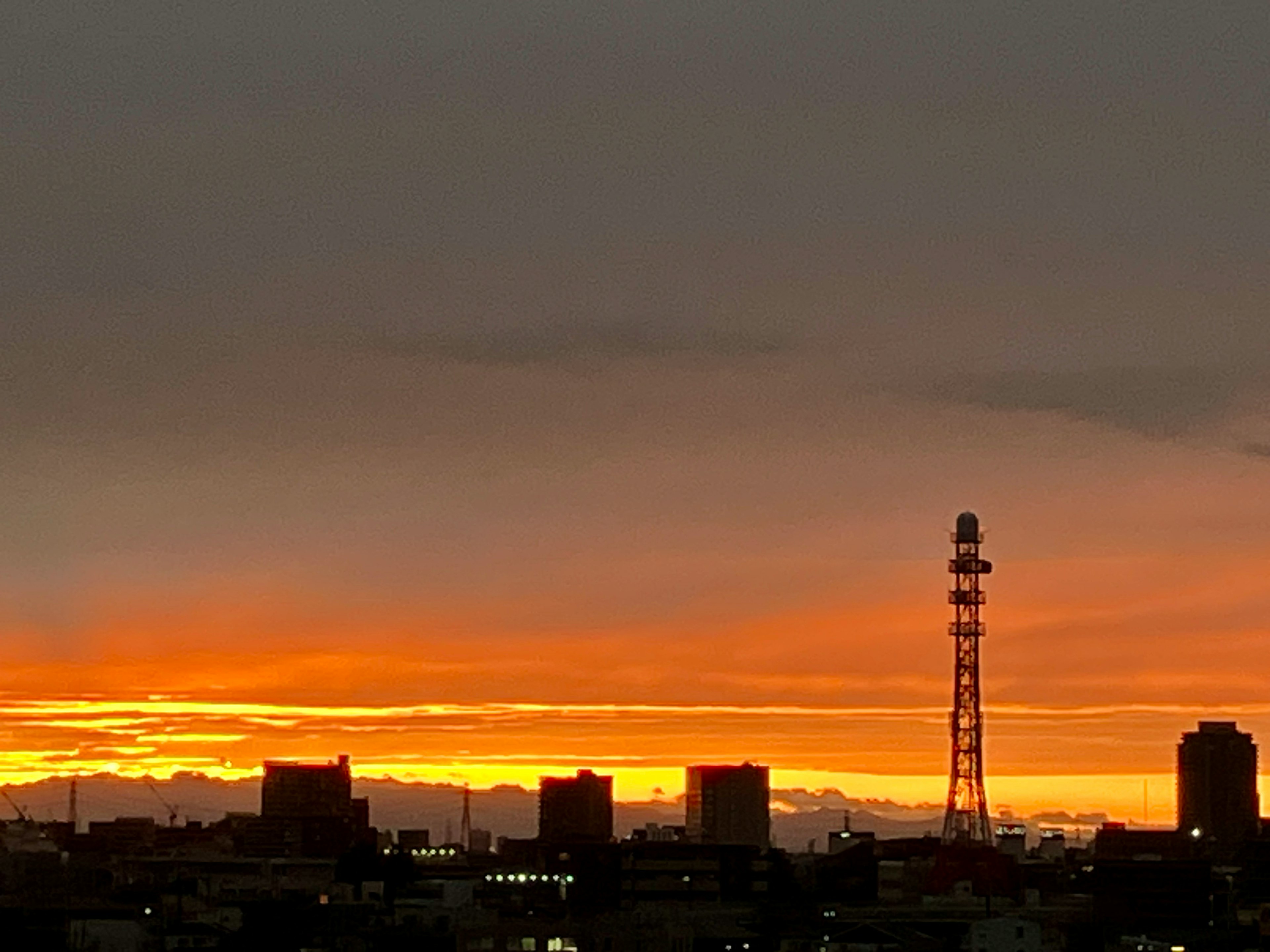 Stadtlandschaft bei Sonnenuntergang mit silhouettierten Gebäuden und einem Sendemast