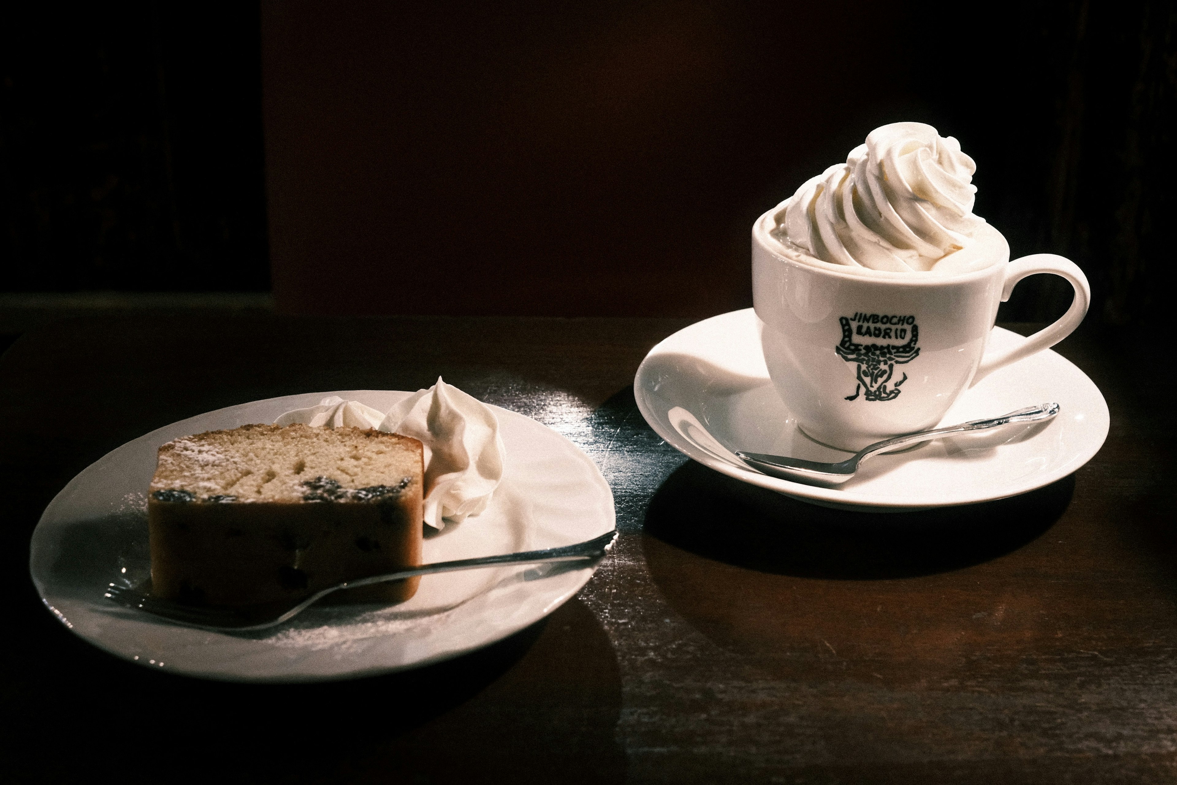 Una scena con una tazza di caffè con panna montata e una fetta di torta su un piatto