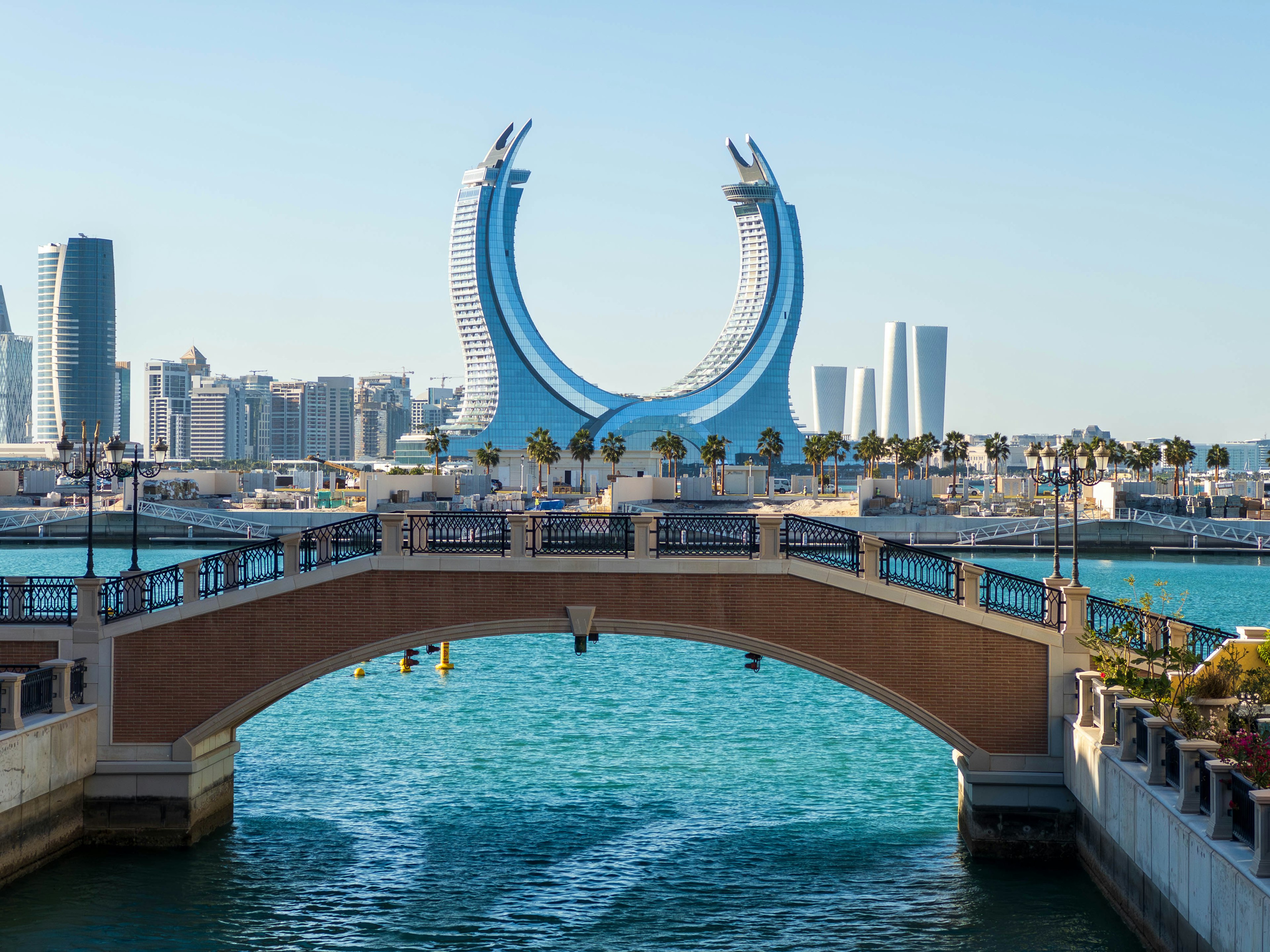 Coastal view featuring a blue arch-shaped building and a bridge in Doha