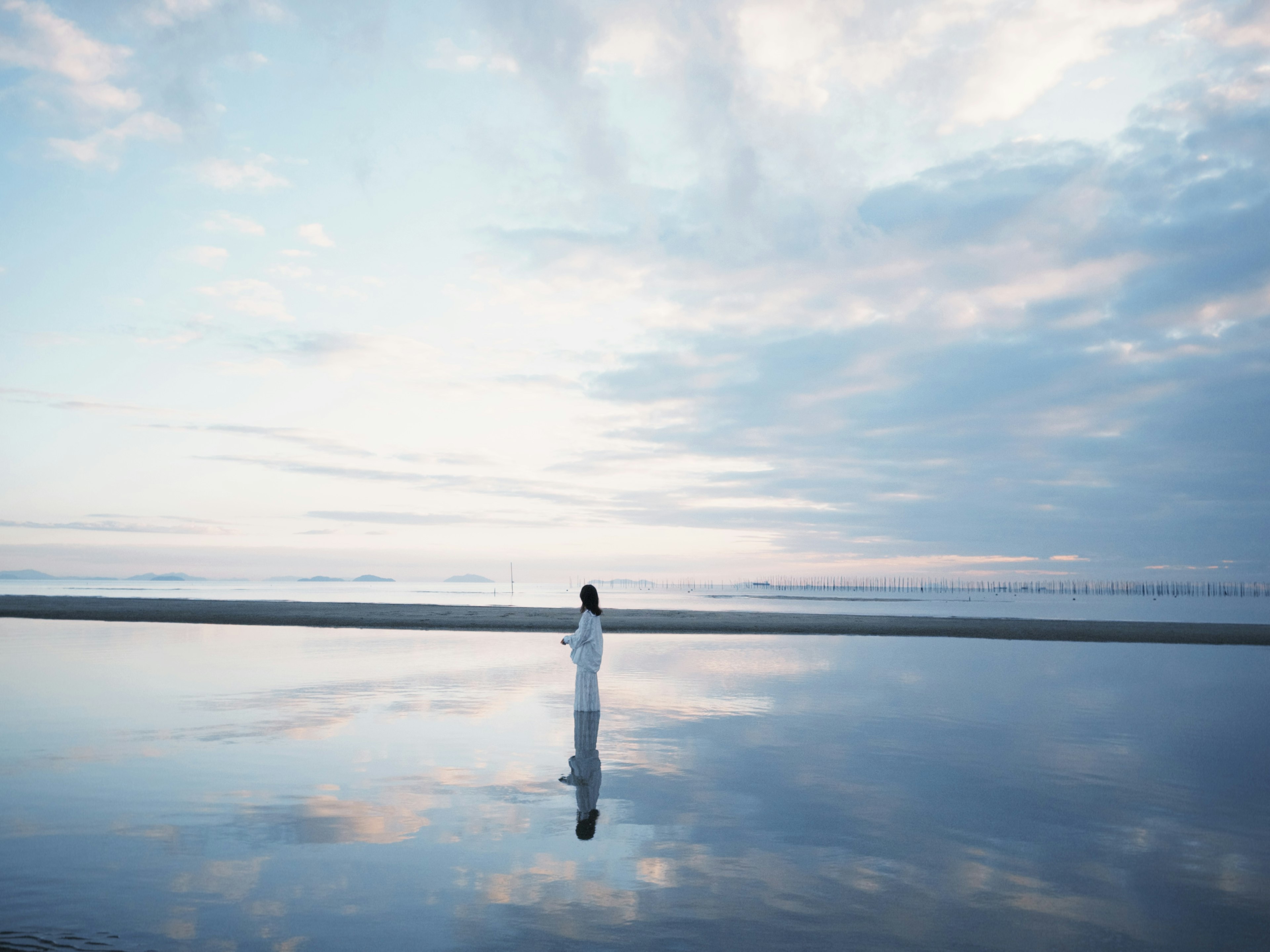 静かな海の反射に立つ白い服の人物