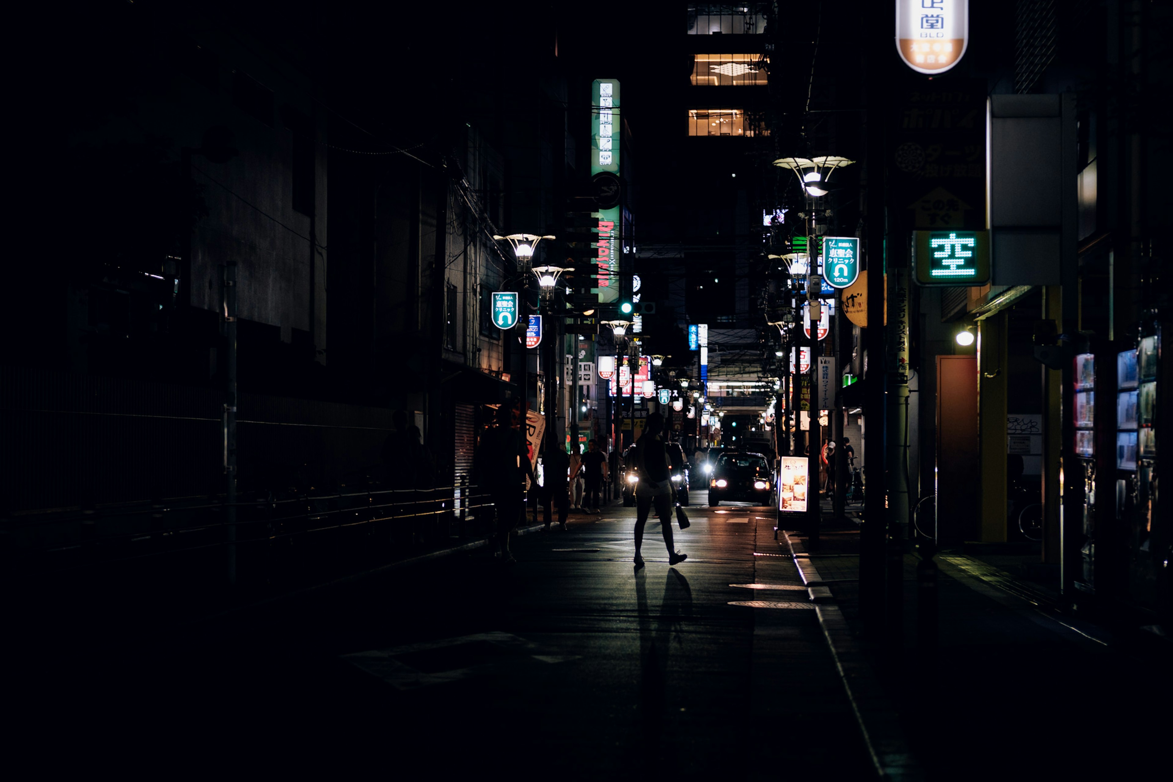 Calle débilmente iluminada con letreros de neón y siluetas