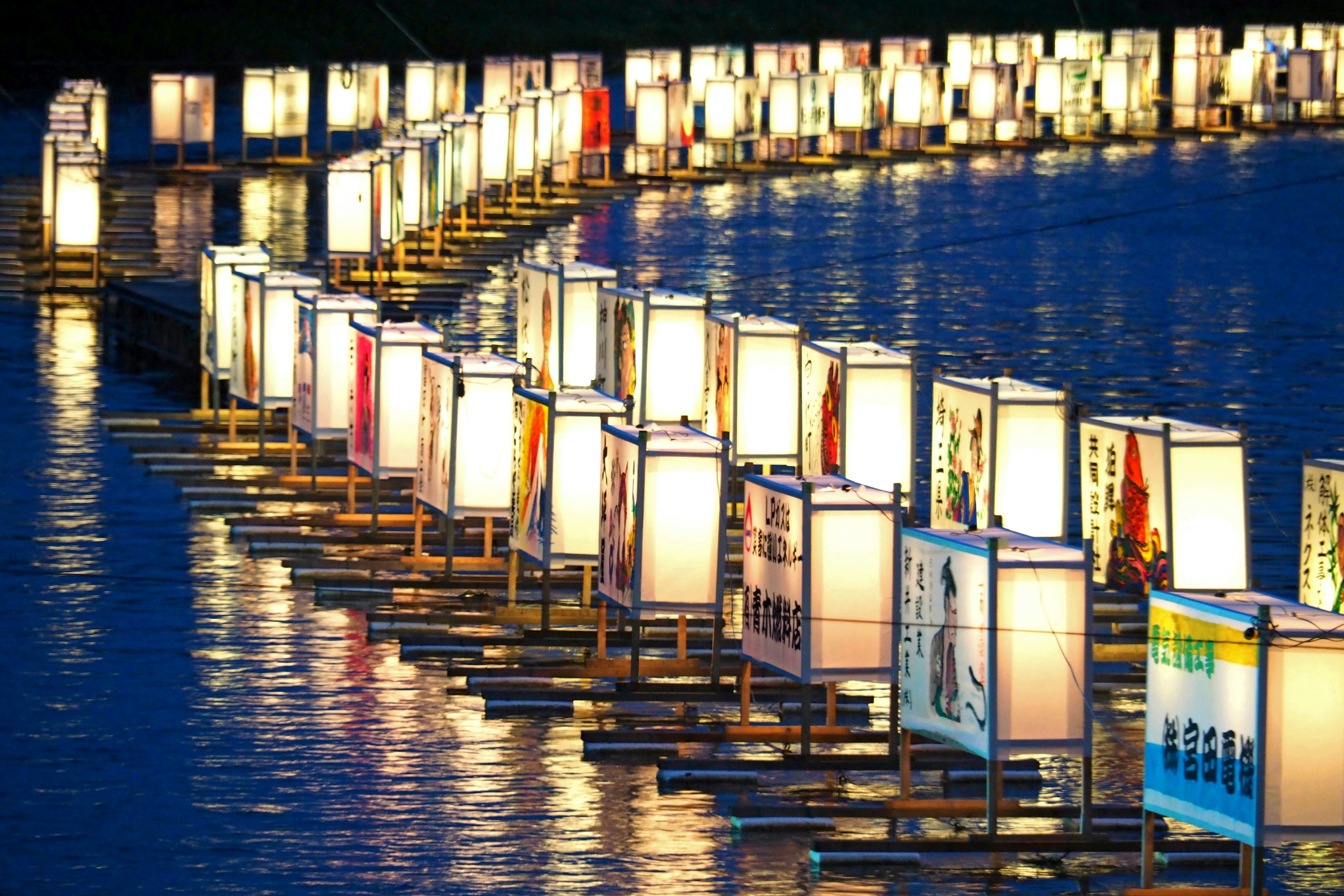 Row of illuminated lanterns reflecting on water with a serene blue backdrop