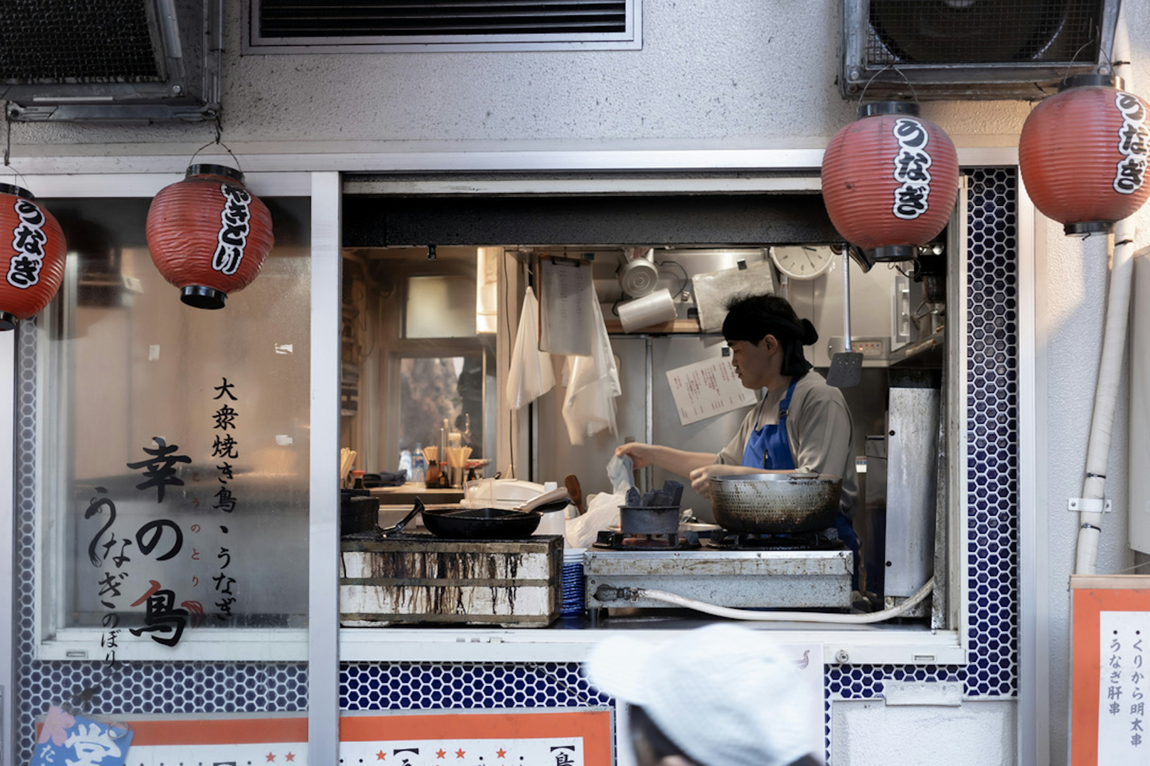 小さな日本の食堂で料理をする女性の姿と赤い提灯