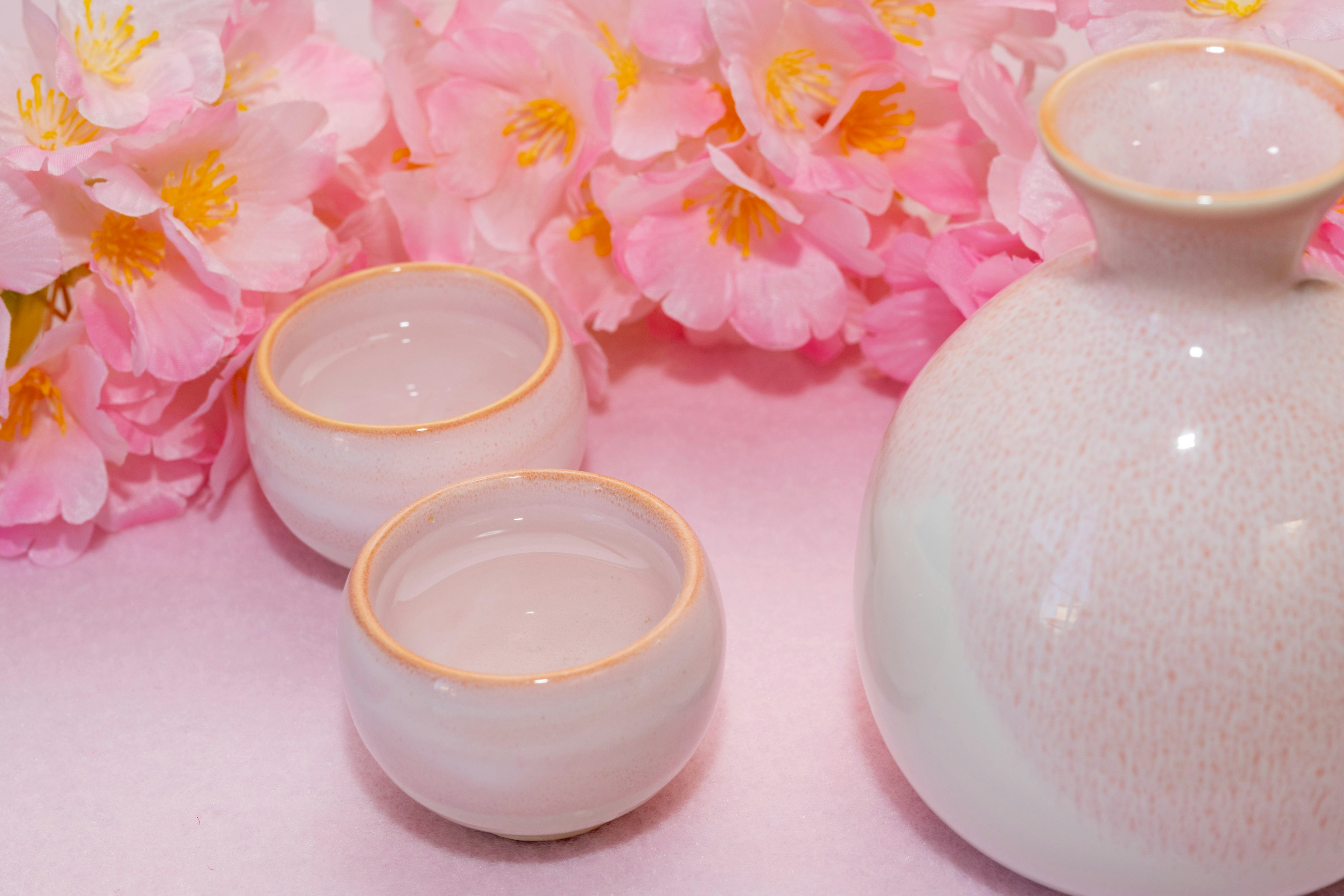 Set di sake in ceramica bianca con piccole coppe su uno sfondo floreale rosa