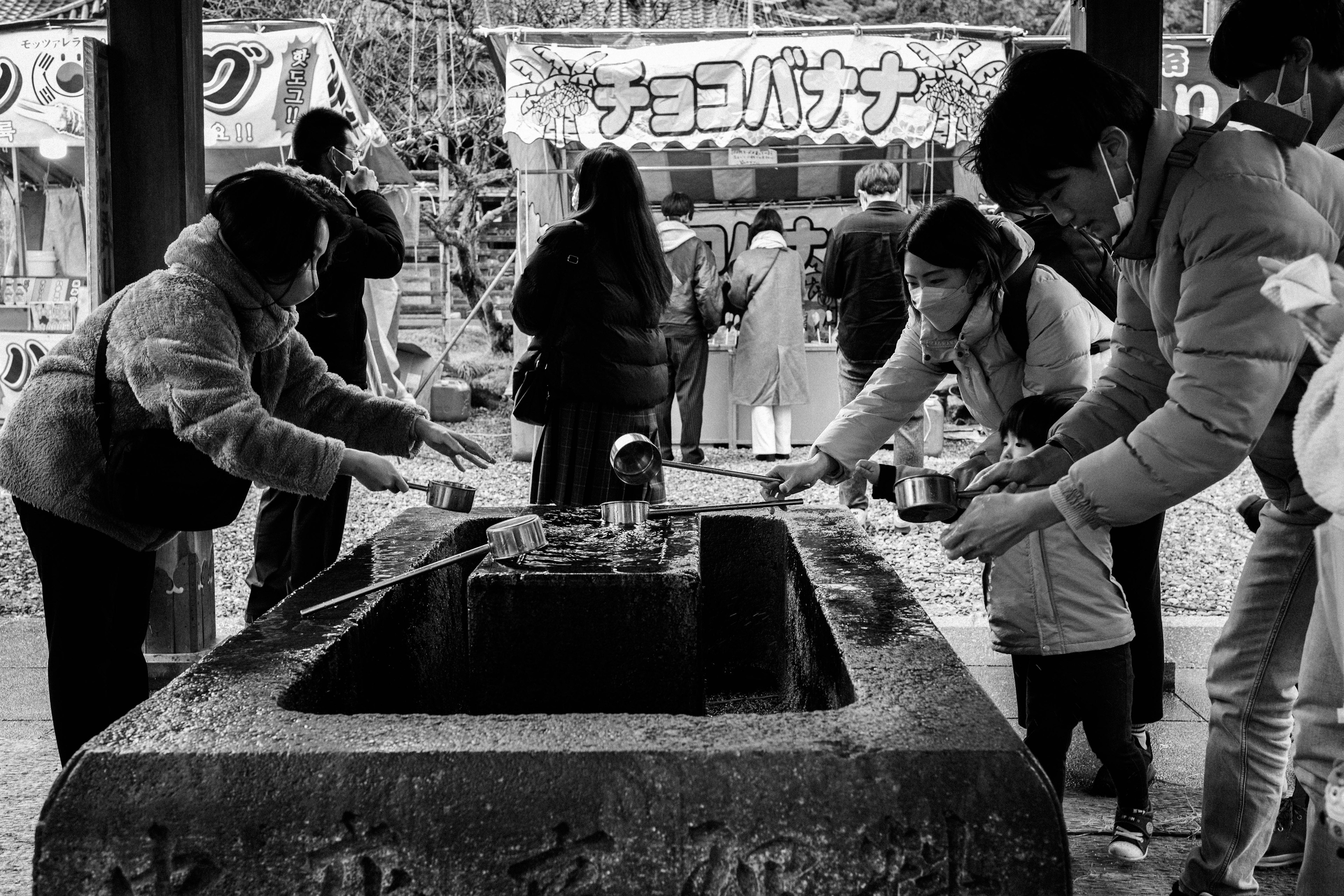 黒白の風景で、参拝者たちが手水舎で水を使っている様子