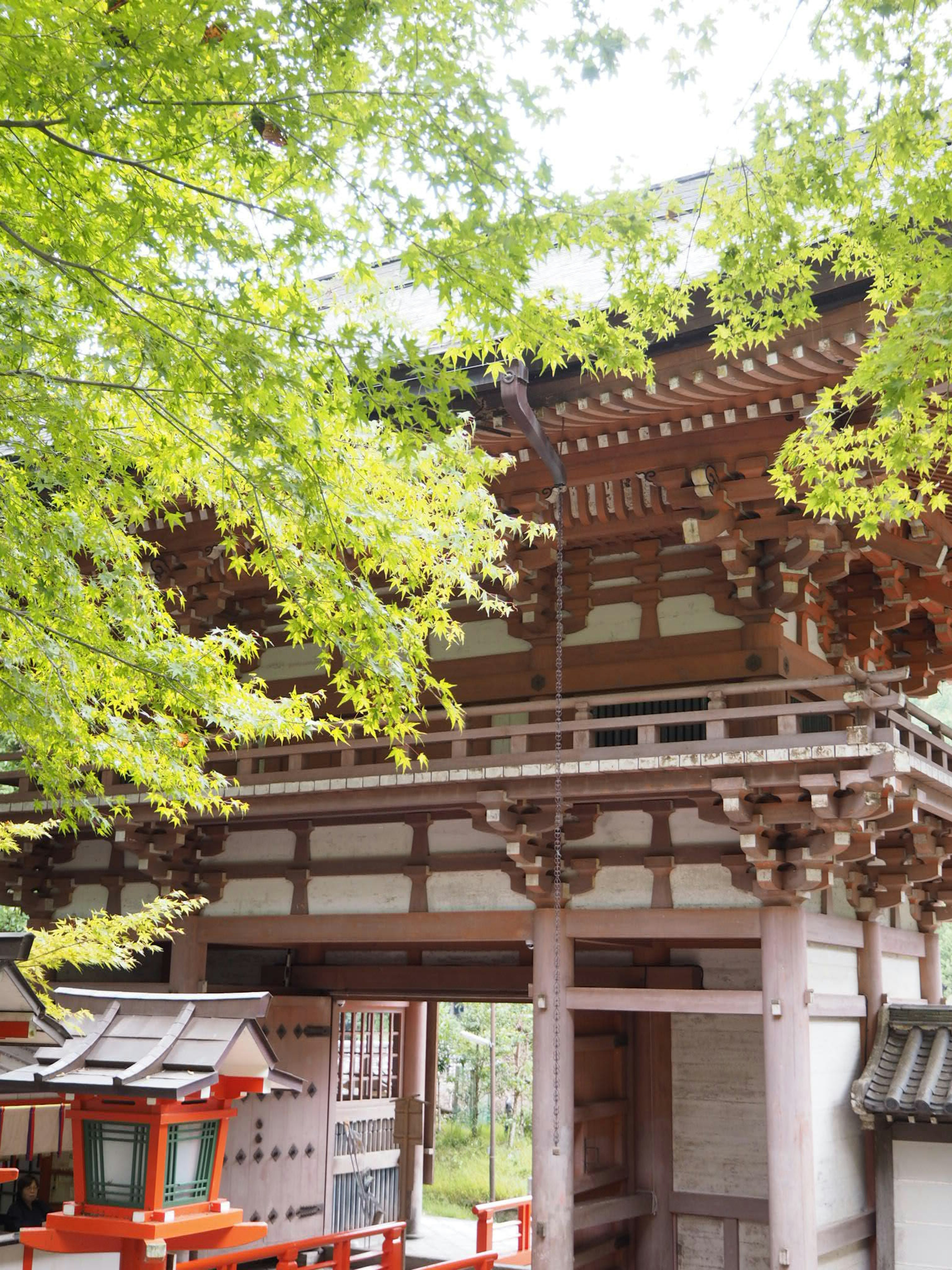 Traditionelles japanisches Tempeltor umgeben von grünen Bäumen rotes Torii sichtbar