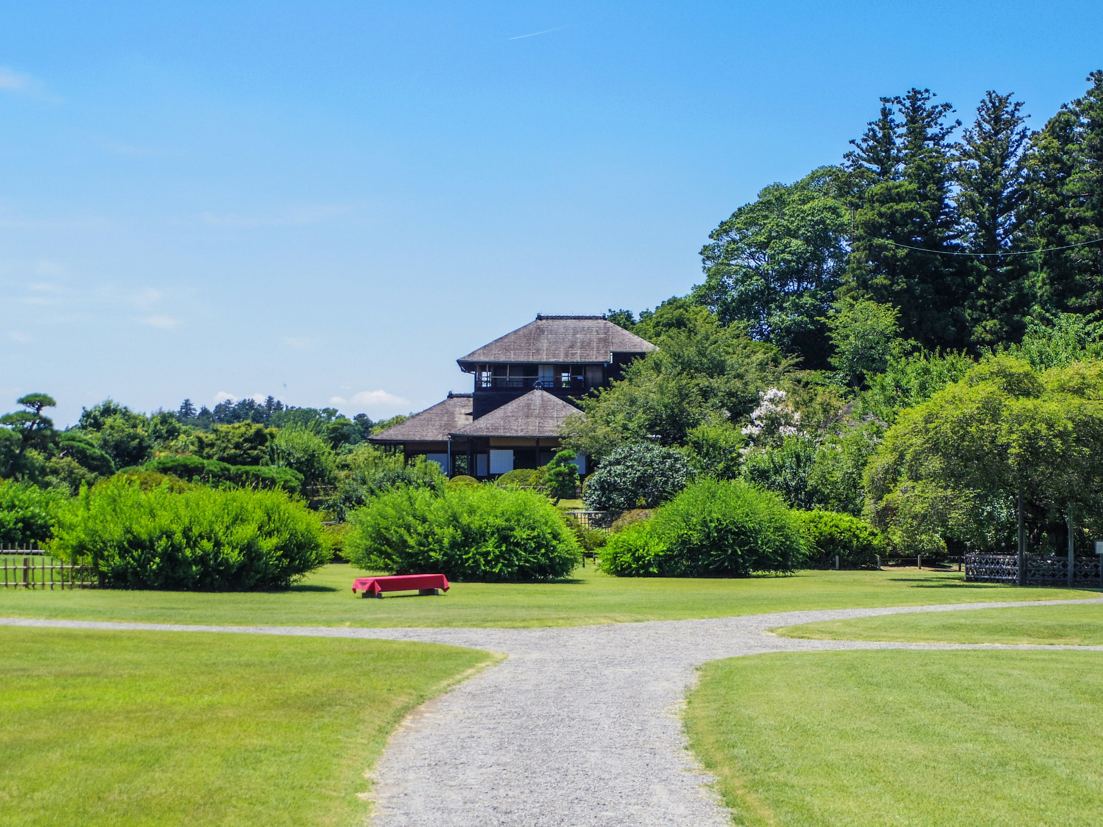 Traditionelles japanisches Haus umgeben von üppigem Grün und einer roten Bank